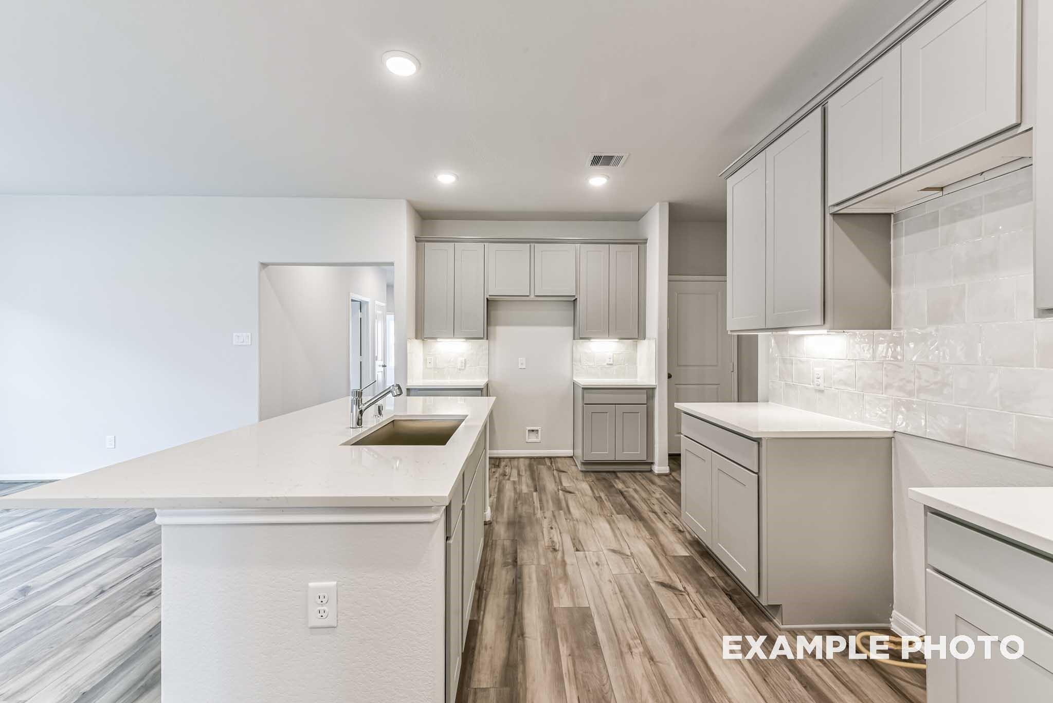Modern kitchen with gray cabinets, quartz countertops, and wood-look flooring in The Laguna C home, Sunterra, Katy, Texas.