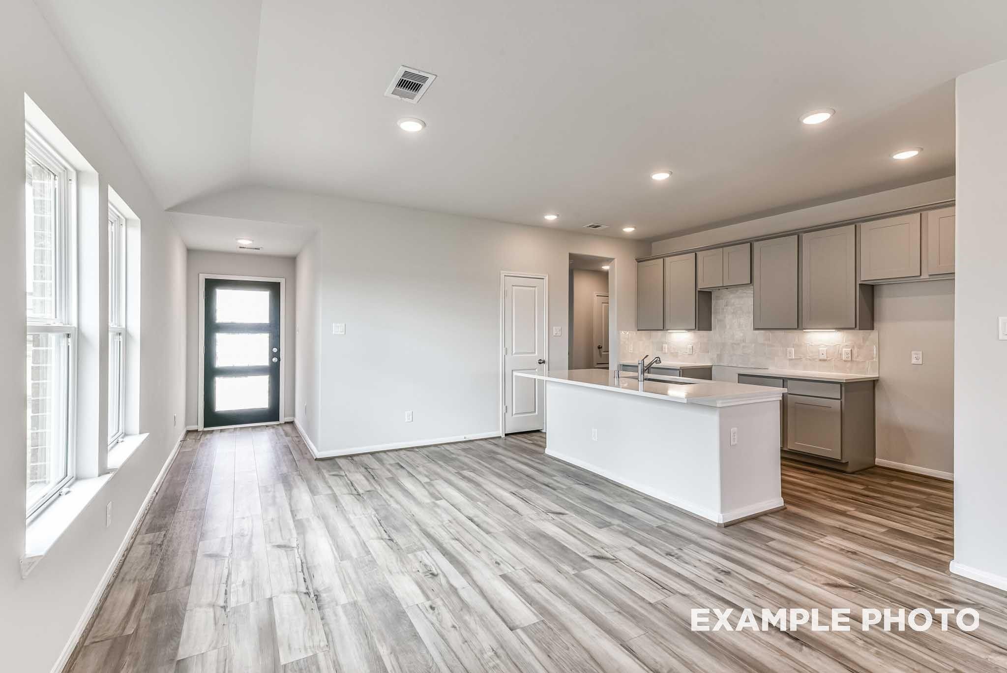 Open-concept living and kitchen with white island, gray shaker cabinets and vinyl plank flooring in Davidson Homes The Costa A, Dayton, TX
