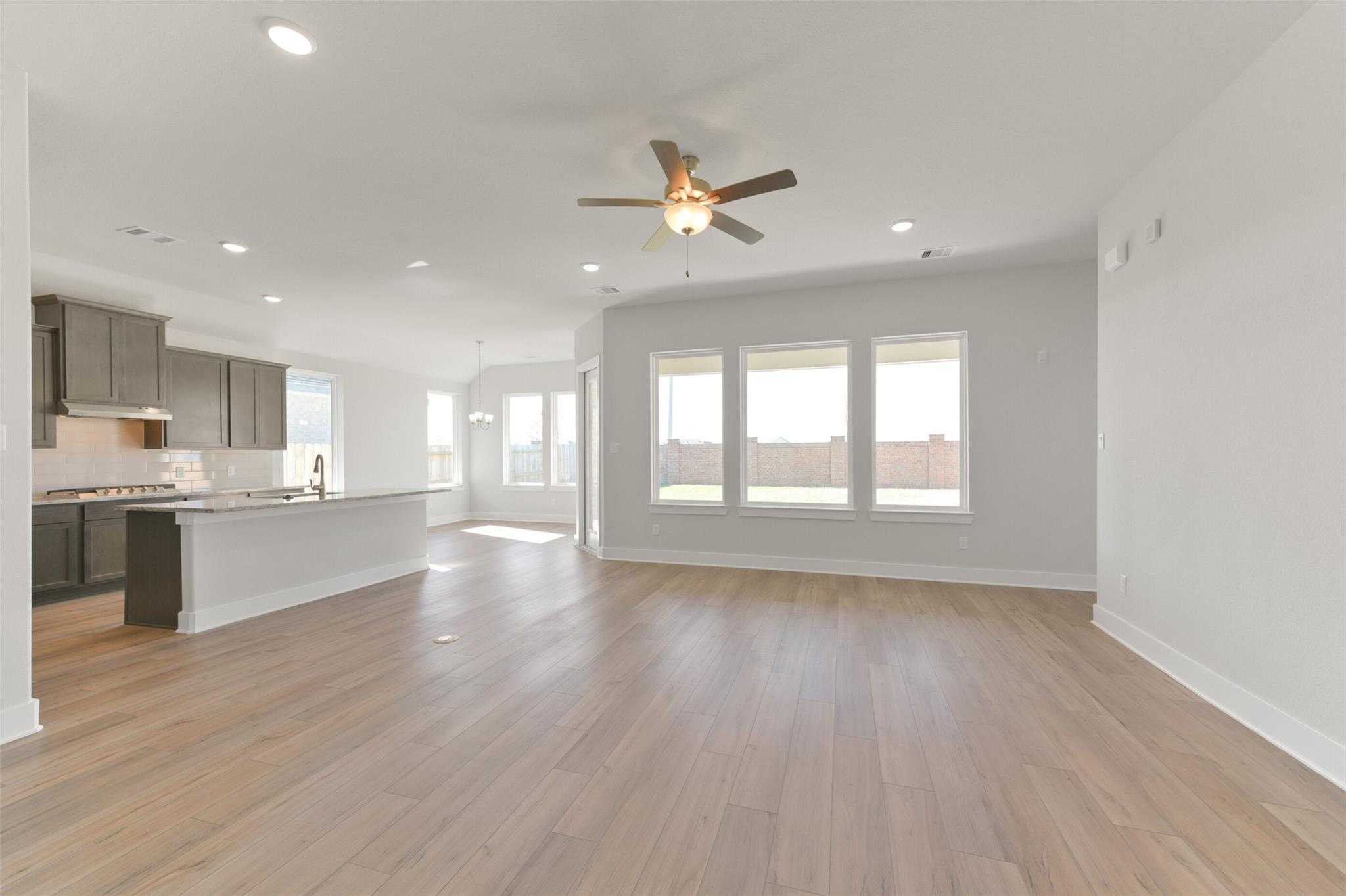 Bright open-concept kitchen-living area with white island, wood floors, large windows, ceiling fan in Davidson Homes The Diana A, Texas City