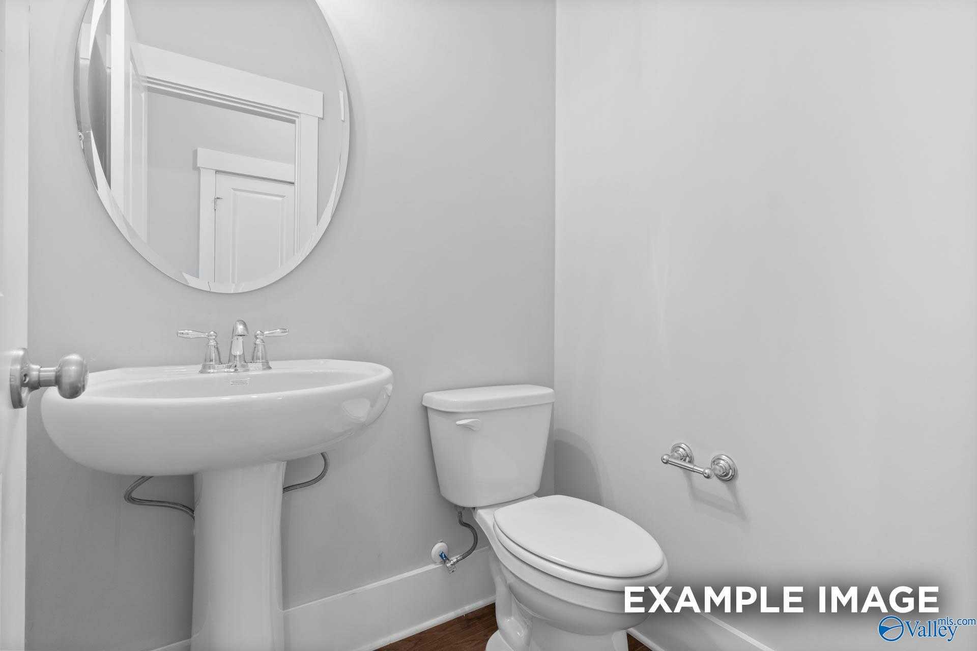 Elegant powder room with white pedestal sink, round mirror, and toilet in Davidson Homes The Rockford, Pikes Ridge, Meridianville, Alabama