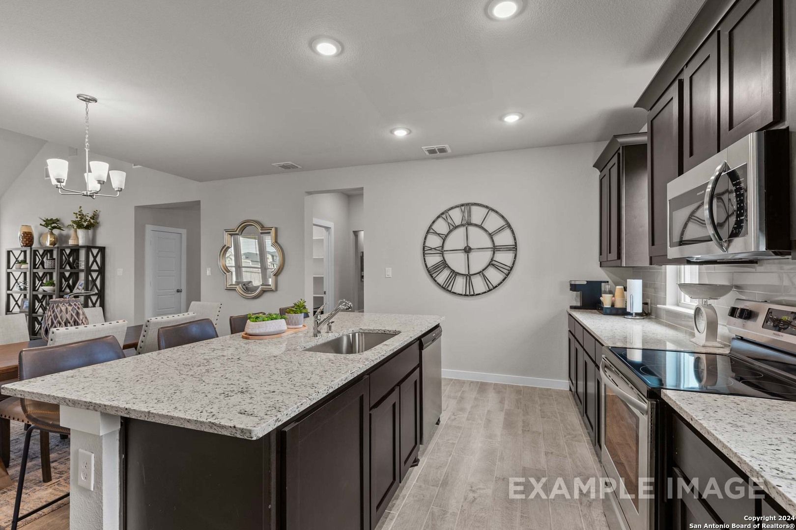 Modern open-concept kitchen with granite countertops, dark cabinets, stainless appliances in The Collin A by Davidson Homes, Seguin, Texas