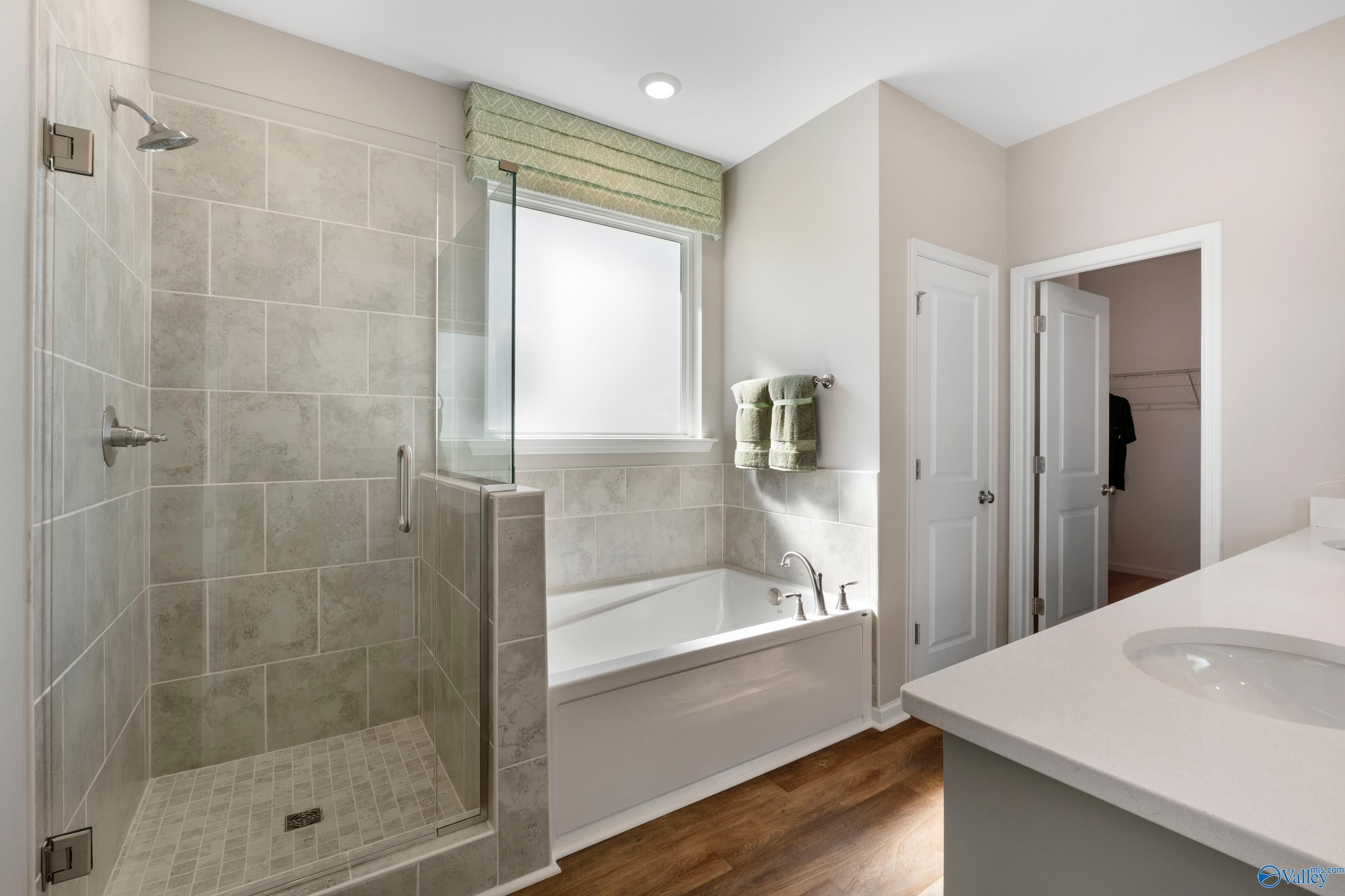 Elegant master bathroom featuring glass-enclosed shower, soaking tub, quartz vanity, and walk-in closet in Davidson Homes The Stella, Madison, Alabama