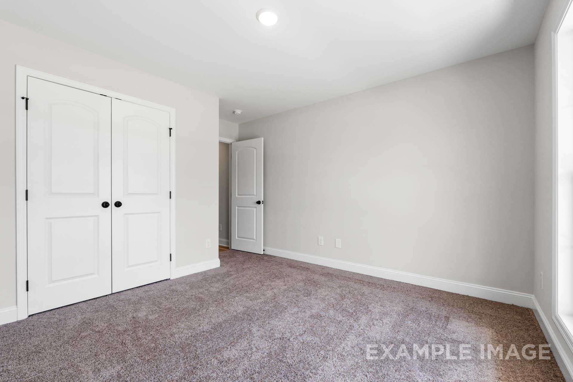 Spacious master bedroom in The Holly M with white bi-fold closet doors, en-suite bath entry, light gray walls, and beige carpet