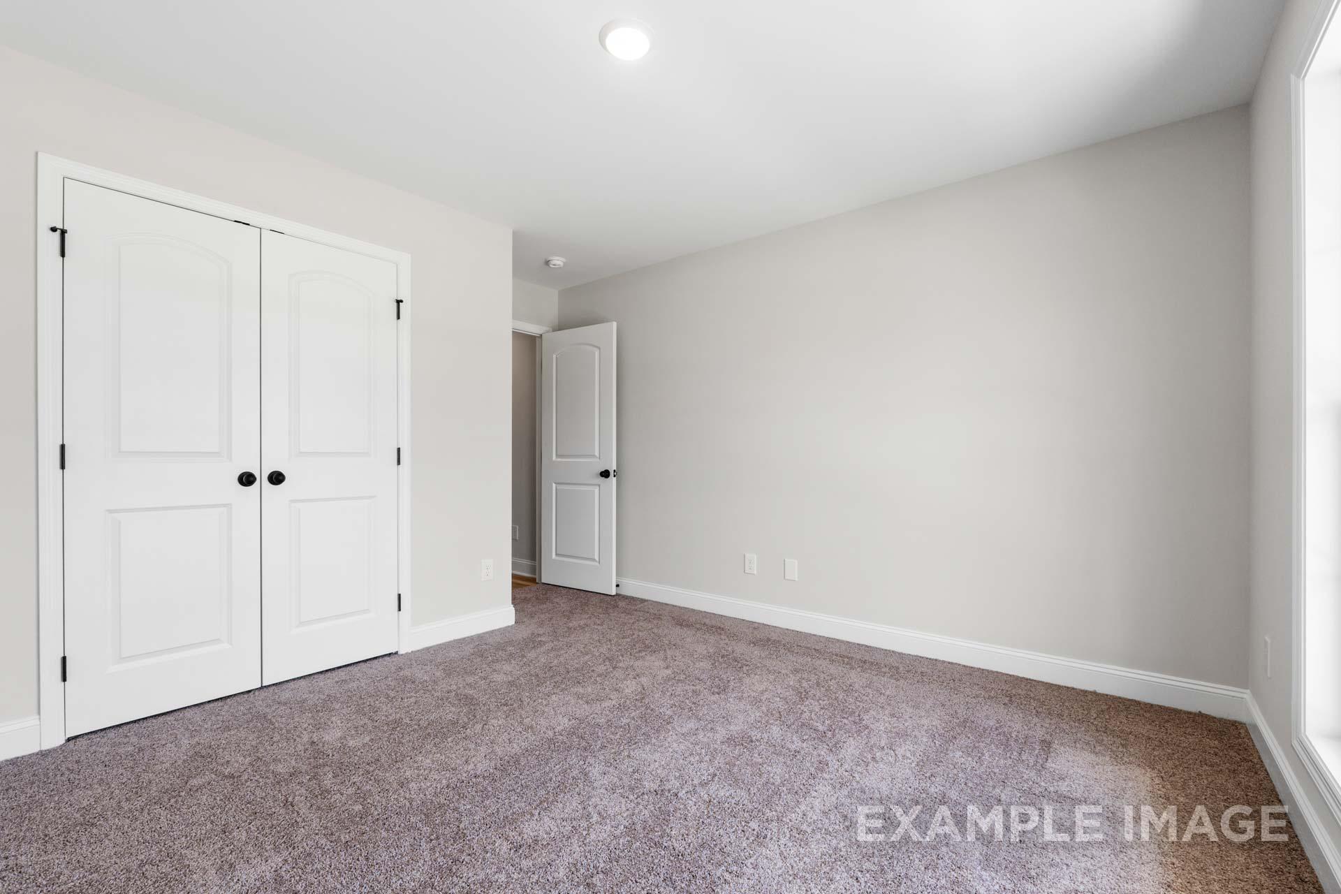 Spacious master bedroom in The Holly M with white bi-fold closet doors, en-suite bath entry, light gray walls, and beige carpet