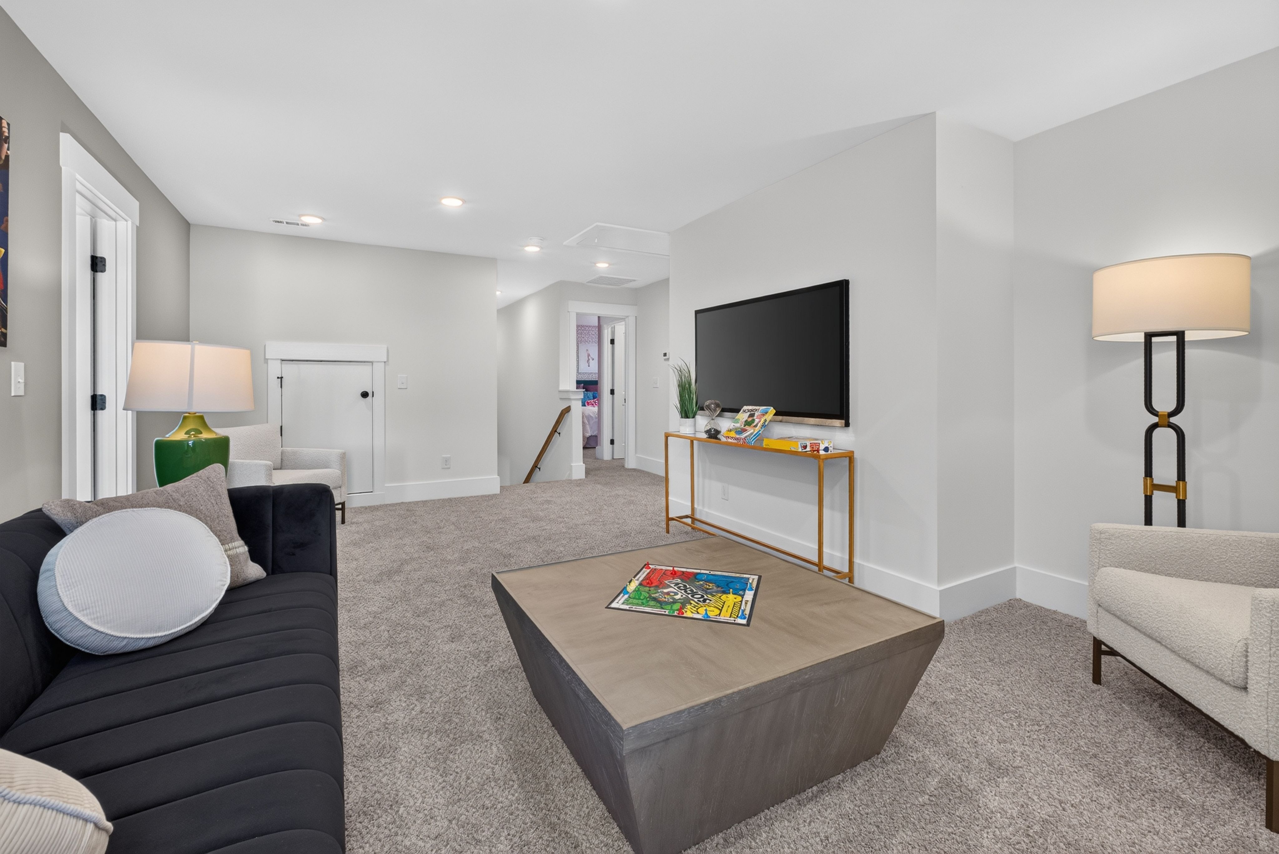 Spacious upstairs bonus room at Evergreen Mill in Madison, AL by Davidson Homes with sofa, wall-mounted TV, and game table