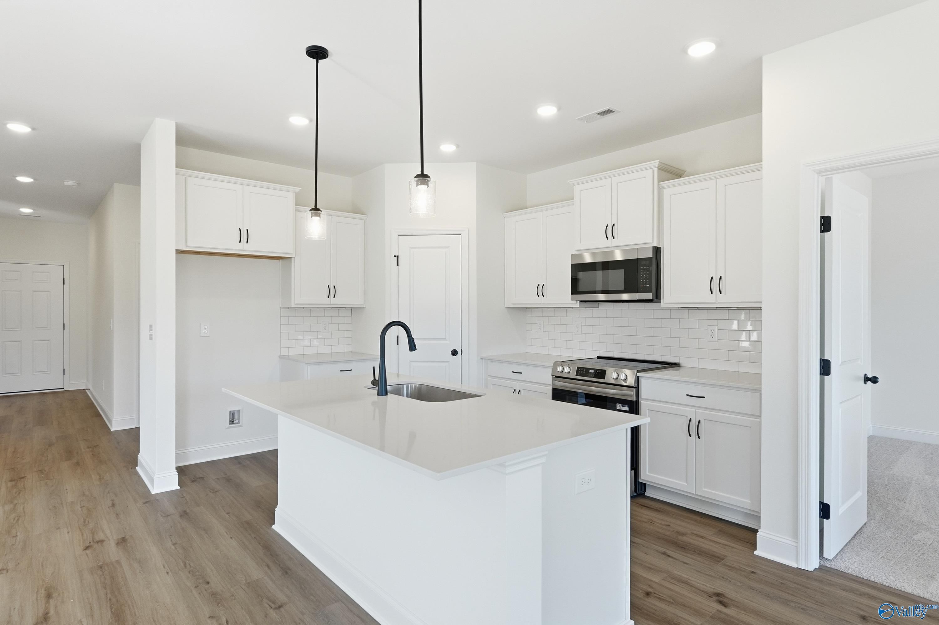 Modern white kitchen island with sink, stainless steel range, subway tile backsplash in Davidson Homes The Franklin C, New Market, AL