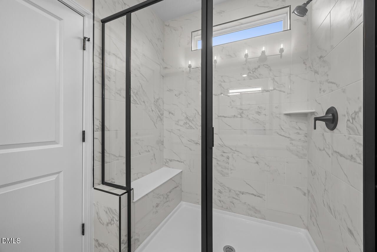 Marble-tiled walk-in shower with glass door, built-in bench, and black fixtures in Davidson Homes The Ashport M Wendell, NC