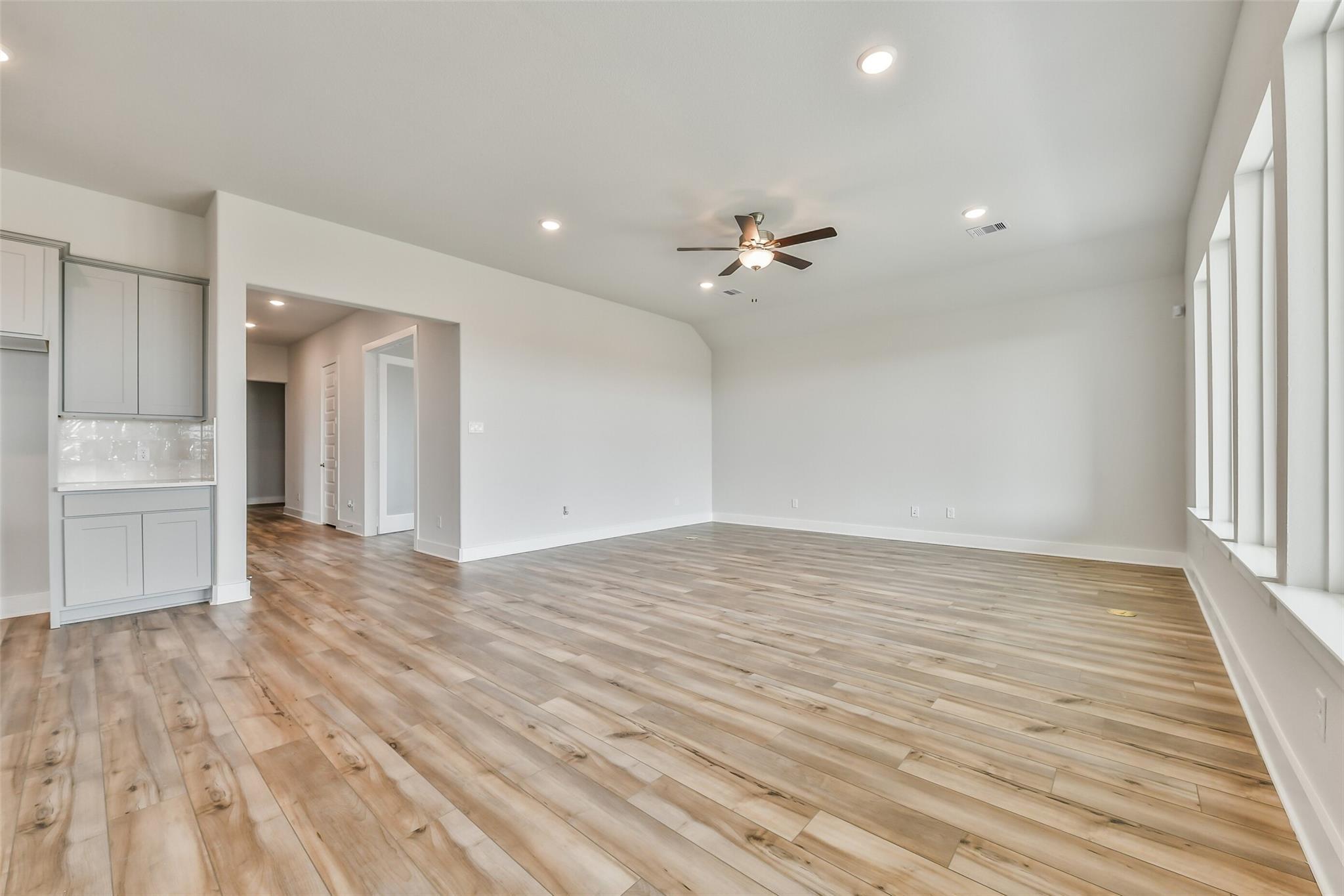 Spacious open living area with hardwood floors, ceiling fan, and kitchen cabinets in Davidson Homes The George A, Lago Mar