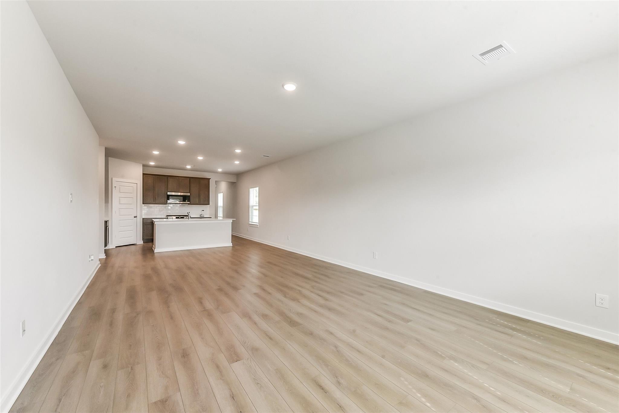 Open kitchen-living space with light oak floors, white island, wood cabinets in Davidson Homes Sabine F, Dayton Texas
