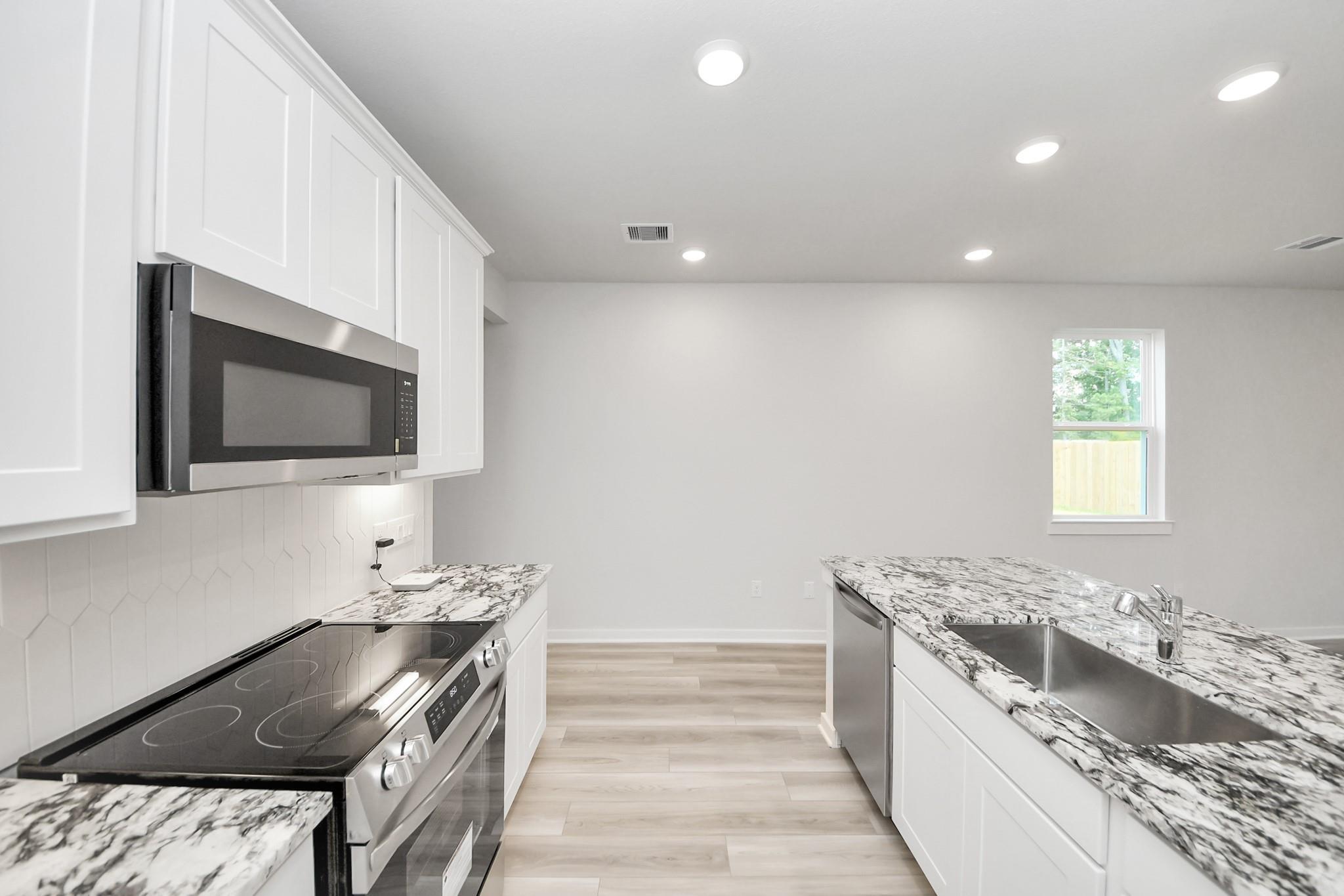 Modern kitchen with granite island and stainless steel appliances in The Sabine F floor plan, Liberty Estates, Texas.