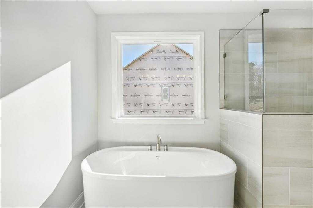 Elegant master bathroom featuring freestanding oval tub, glass shower, and window view in Davidson Homes The Hickory C, Hoschton, GA