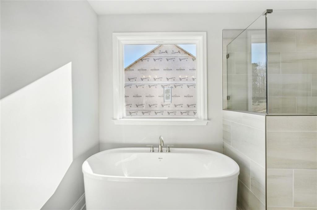 Elegant master bathroom featuring freestanding oval tub, glass shower, and window view in Davidson Homes The Hickory C, Hoschton, GA
