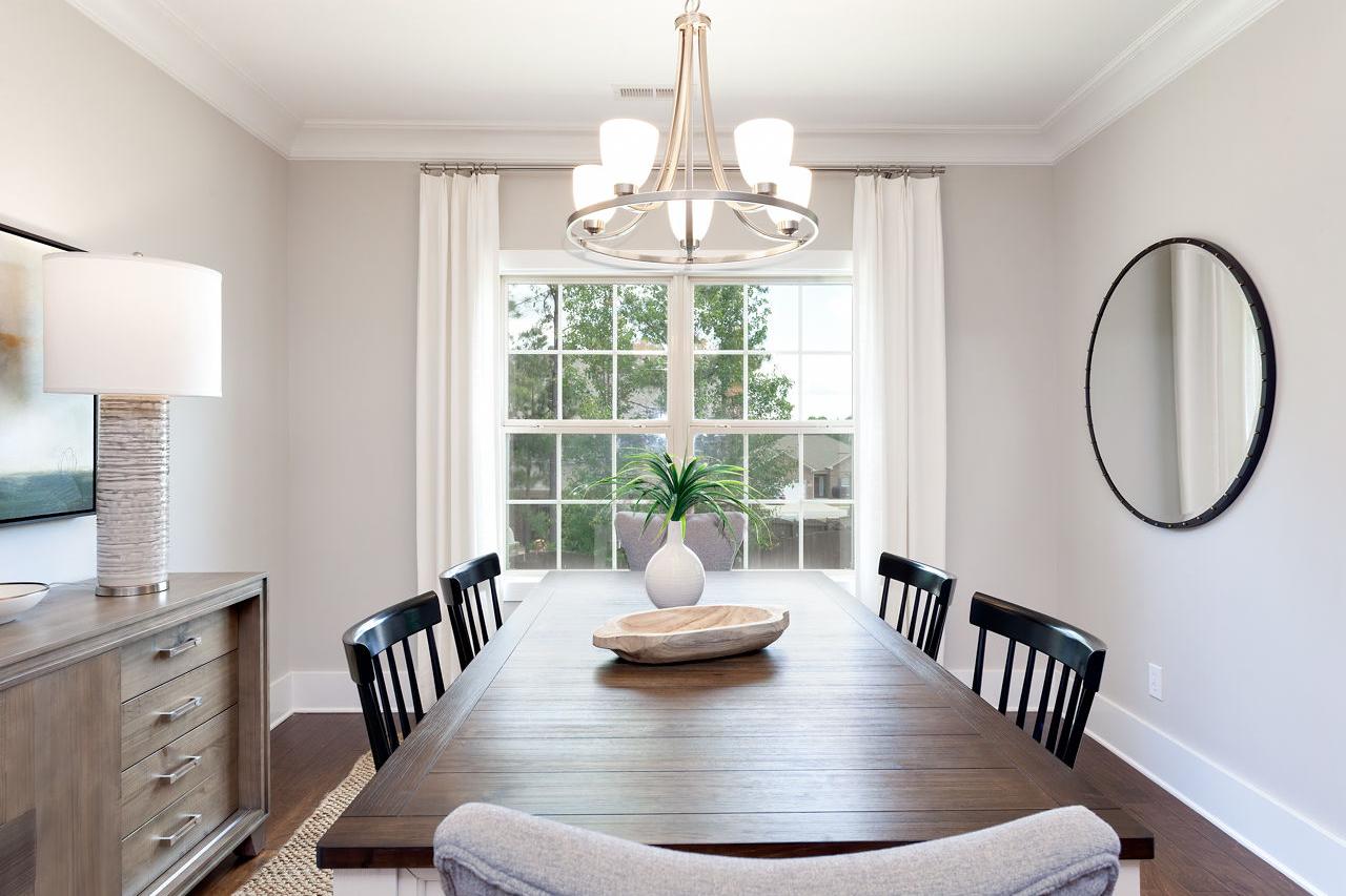 Spacious dining room in The Rockford by Davidson Homes with wooden table, black chairs, chandelier, large window, and round mirror