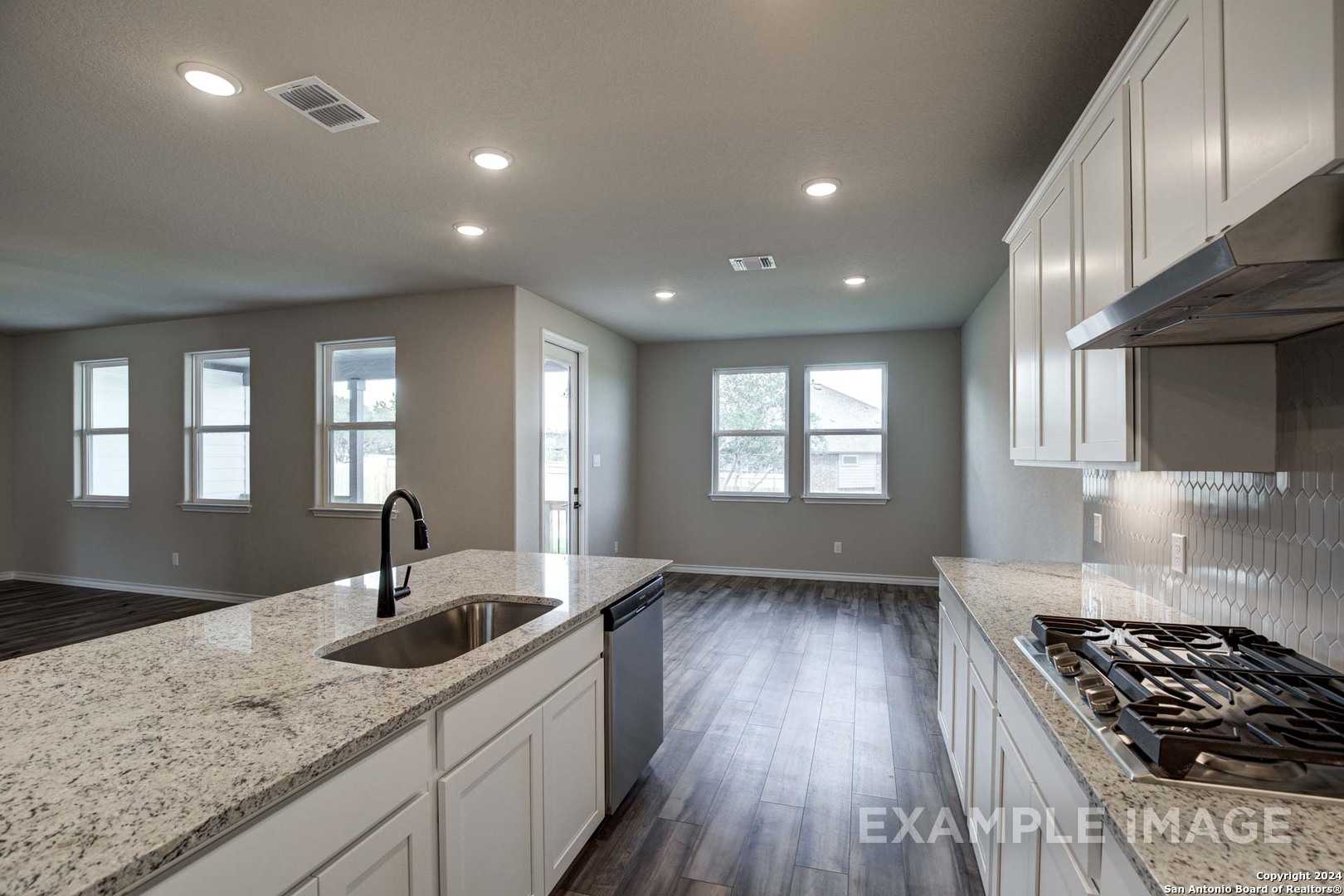 Modern open-concept kitchen with white shaker cabinets, quartz island sink, gas range, and hardwood floors in Davidson Homes The Rockford G, Ladera San Antonio
