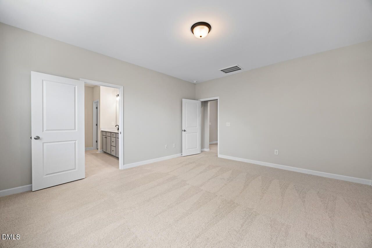 Spacious bedroom with carpeted flooring and attached bathroom in The Chestnut floor plan by Davidson Homes in Aberdeen, NC.