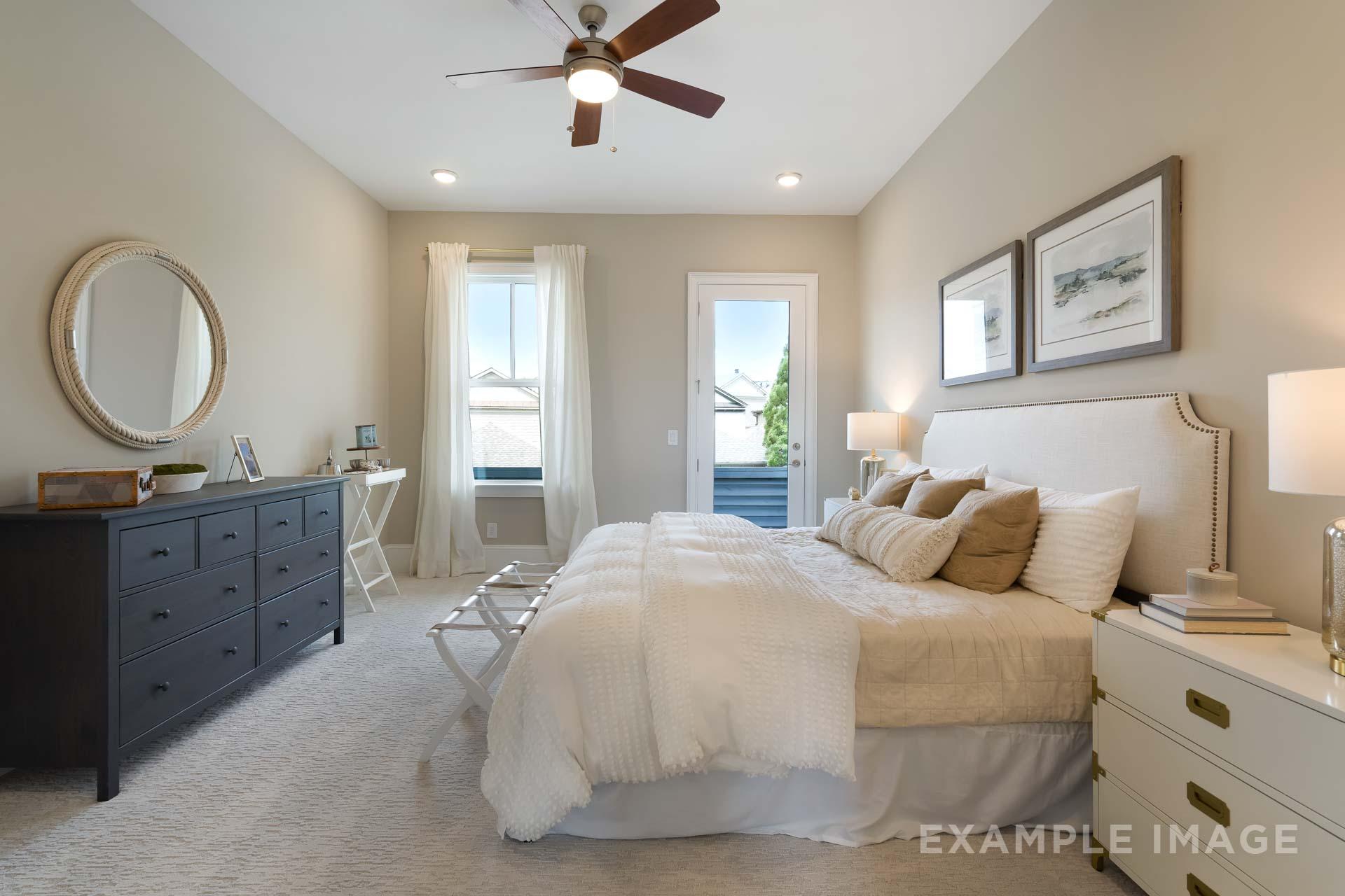 Upper floor master suite in The Seaside home design with king bed, balcony doors, beige walls, and plush bedding