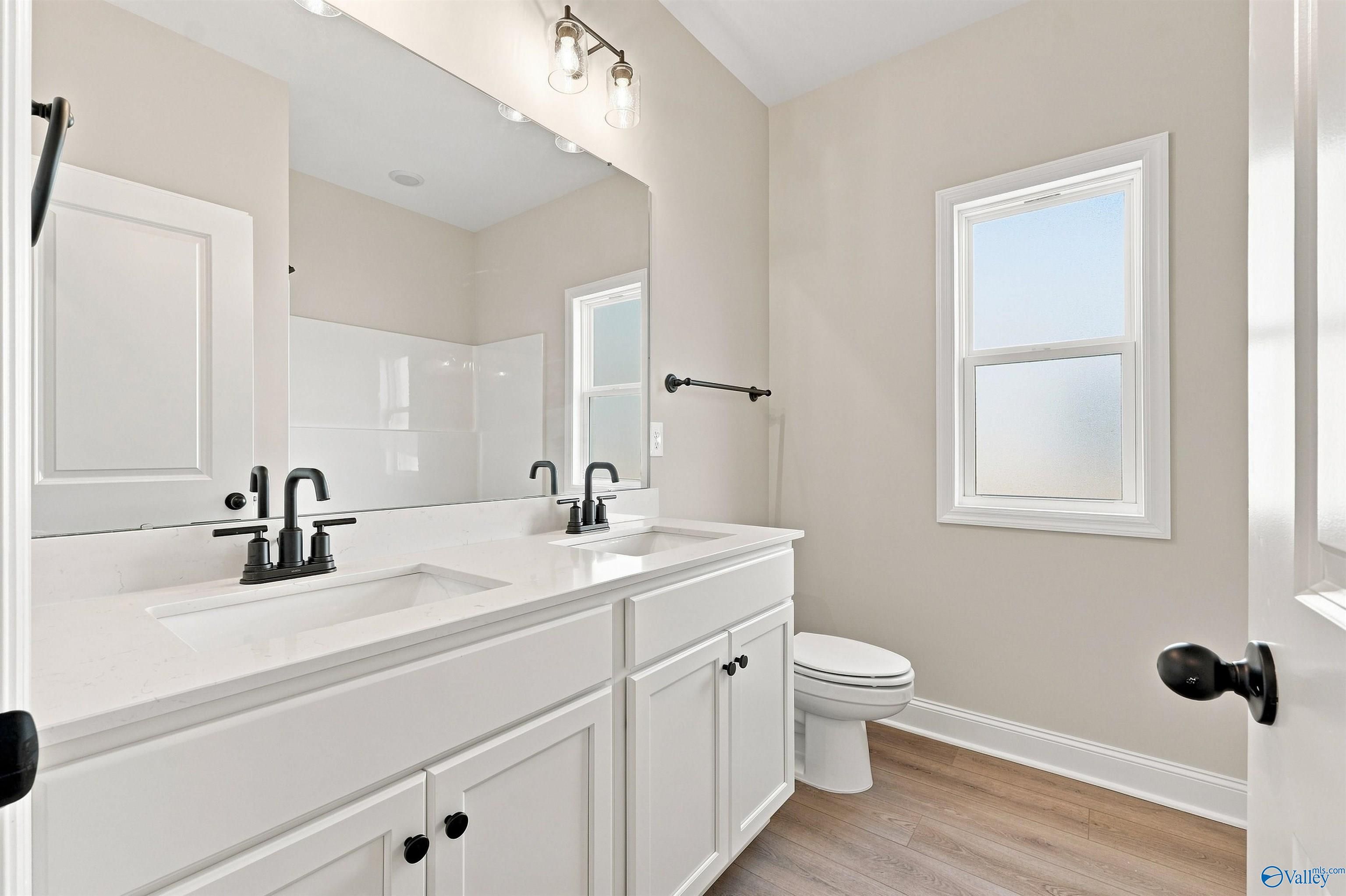 Double vanity bathroom with white cabinetry, matte black fixtures, and wood-look flooring in Davidson Homes The Everett B, Toney AL