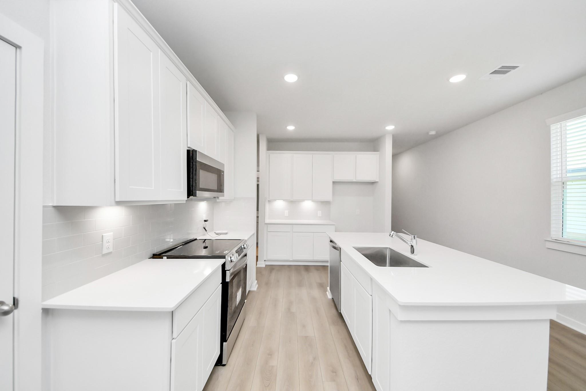 Modern kitchen with white cabinets, quartz countertops, and center island in The Frio F plan at Liberty Estates, Texas.