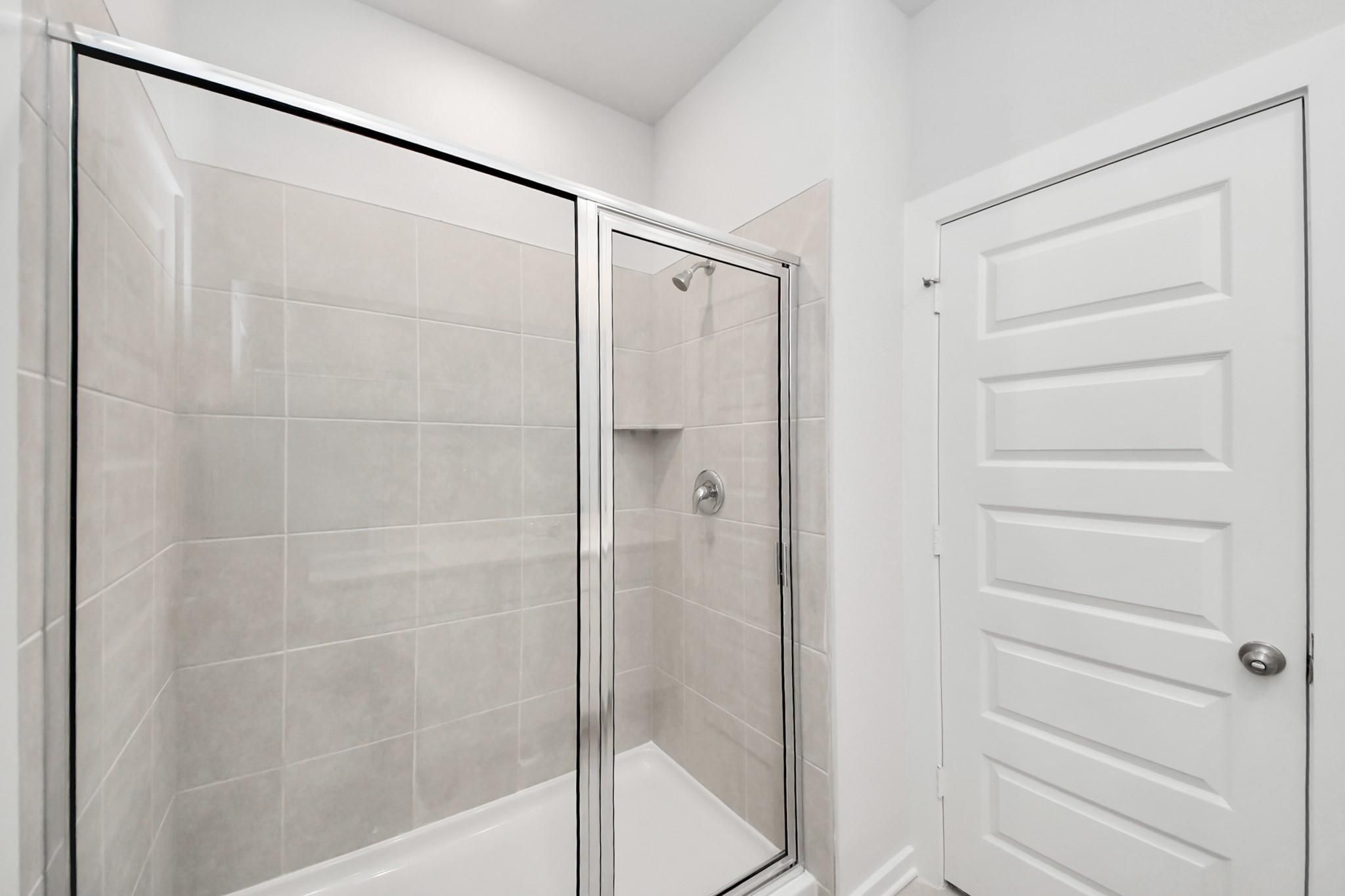 Modern tiled walk-in shower with glass door in The Frio F floor plan at Liberty Estates, Cleveland, Texas.
