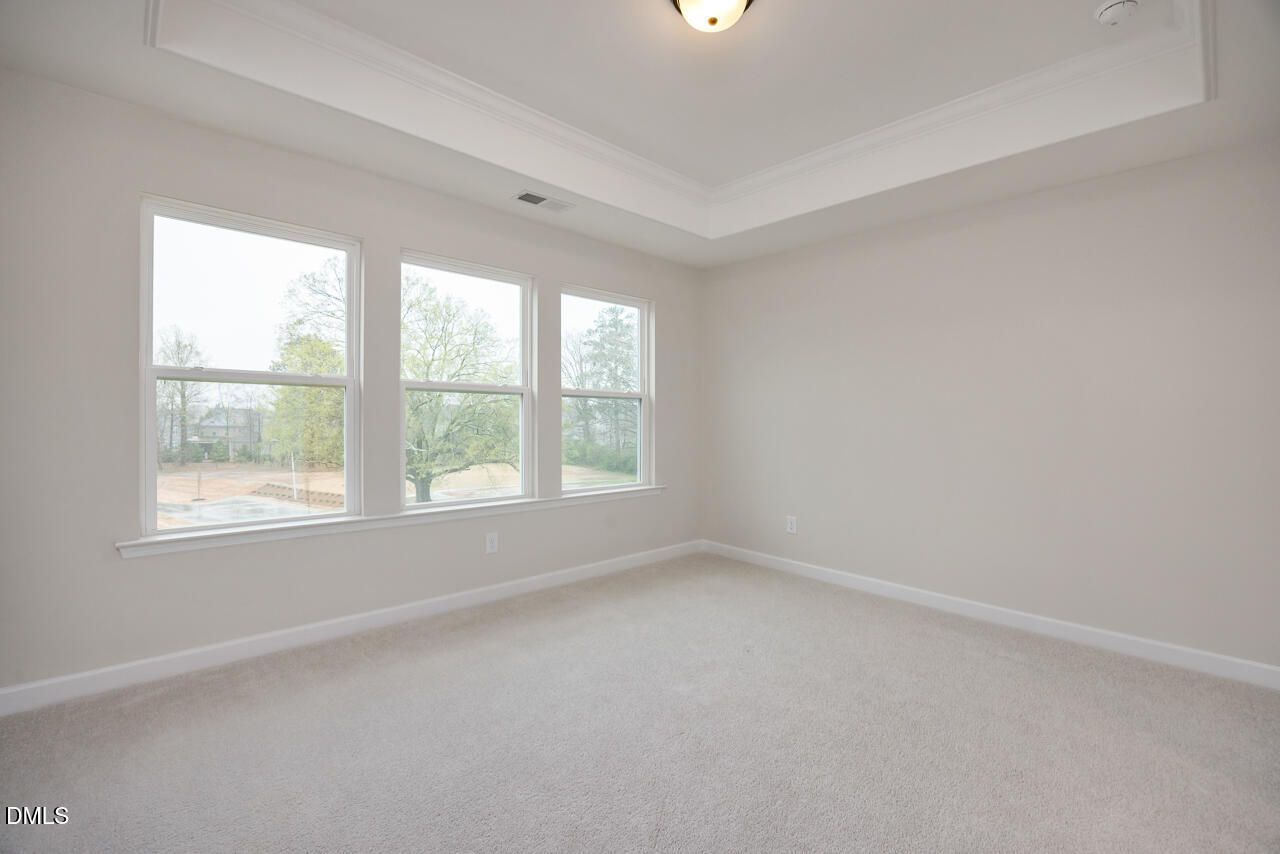 Bright bedroom with tray ceiling, three large windows overlooking trees, beige carpet in Davidson Homes The Mitchell, Knightdale, NC