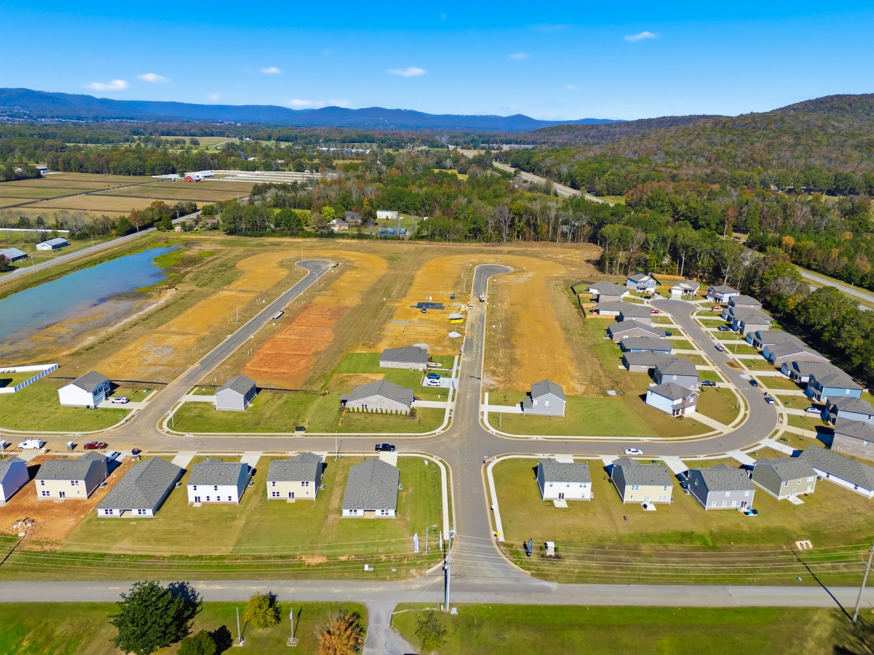 Aerial view of Ramsay Cove neighborhood in Owens Cross Roads Alabama featuring new Davidson Homes, winding streets, pond, fields, and mountain backdrop