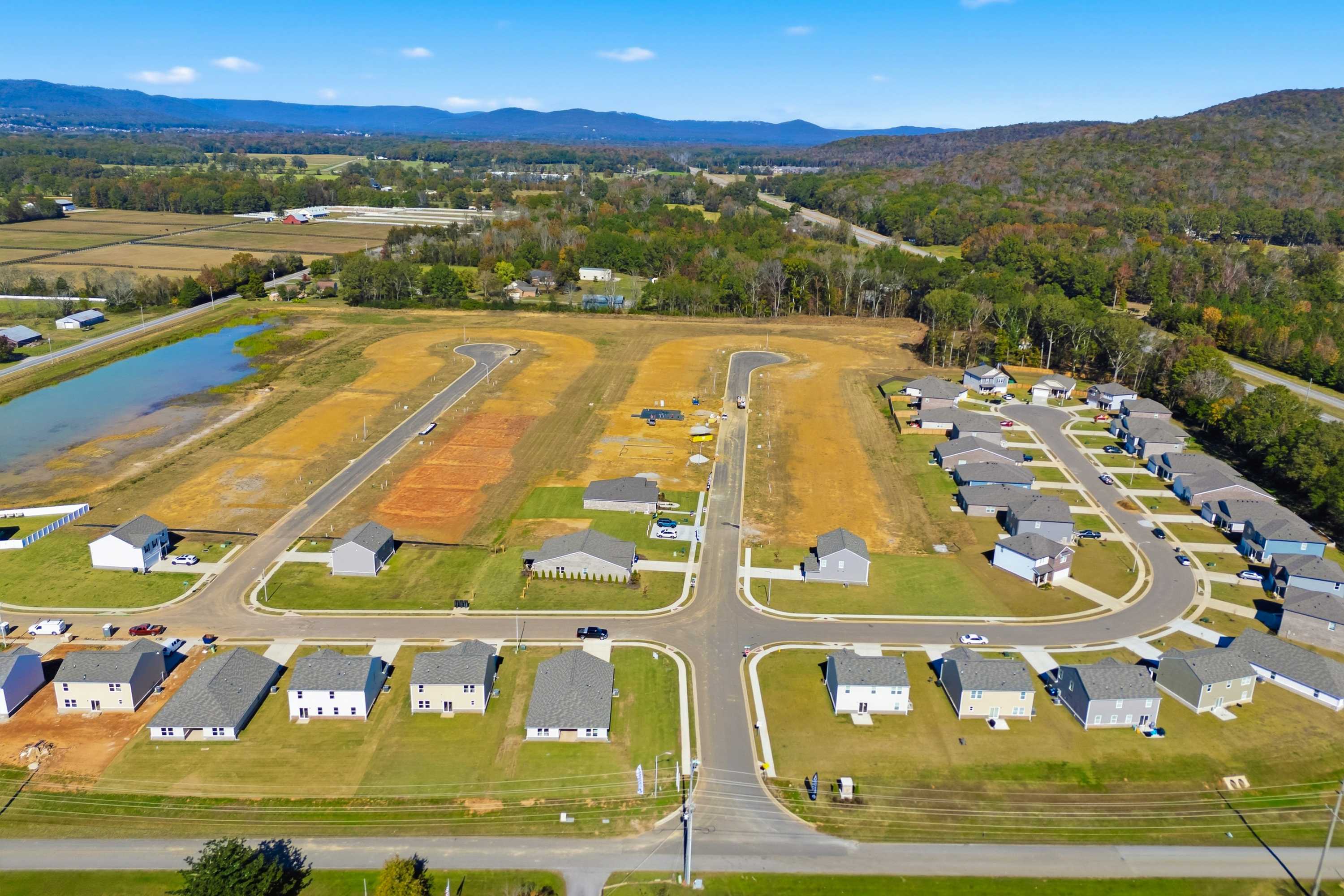 Aerial view of Ramsay Cove neighborhood in Owens Cross Roads Alabama featuring new Davidson Homes, winding streets, pond, fields, and mountain backdrop