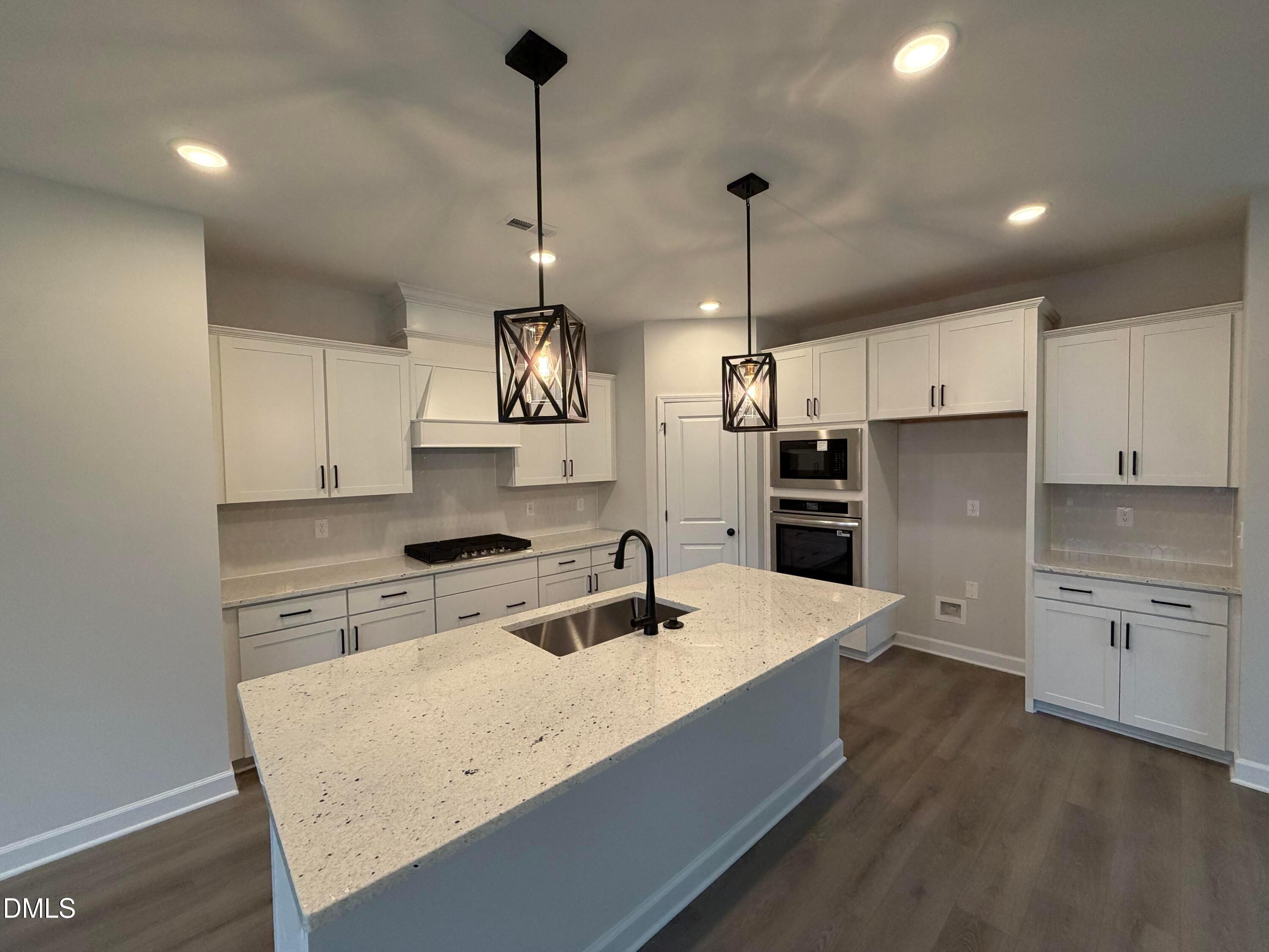Modern kitchen with white shaker cabinets, quartz island, black pendant lights, and stainless appliances in Davidson Homes Preston C plan, Wendell NC