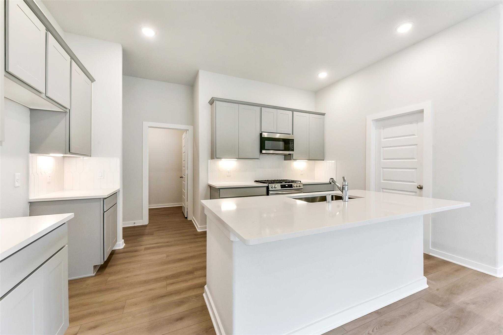 Modern open-concept kitchen with white shaker cabinets, quartz island, and stainless steel appliances in The Laguna C home, Rosharon, Texas