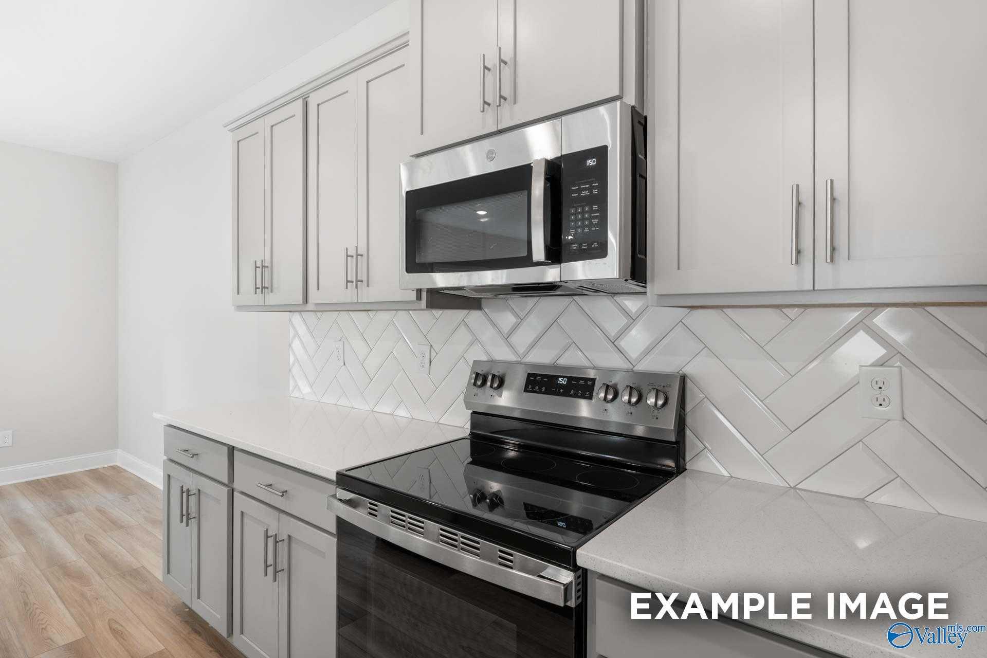 Modern kitchen featuring white shaker cabinets, stainless steel oven and microwave, herringbone subway tile backsplash in The Camden by Davidson Homes, Huntsville