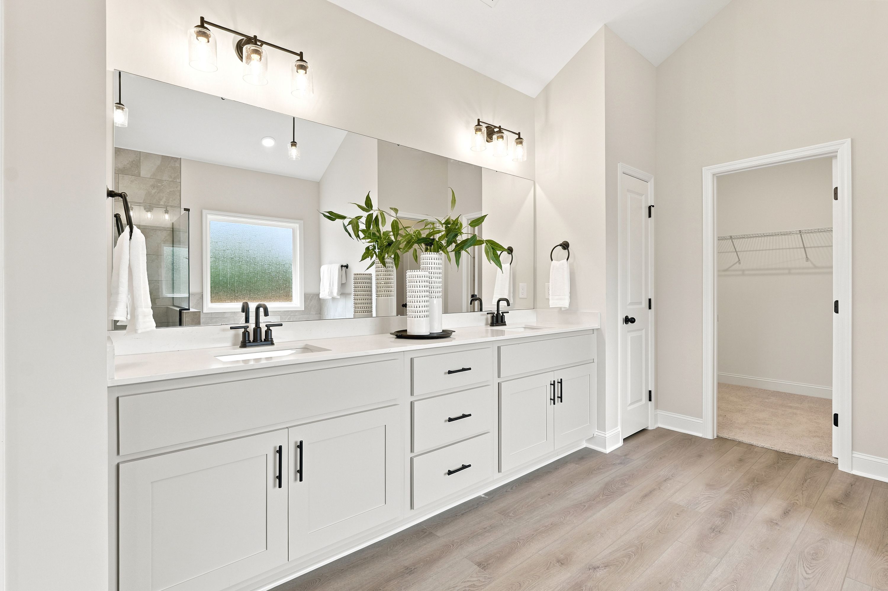 Modern primary bathroom at Riverton Preserve in Huntsville, AL, featuring dual vanities, quartz countertops, and walk-in closet.