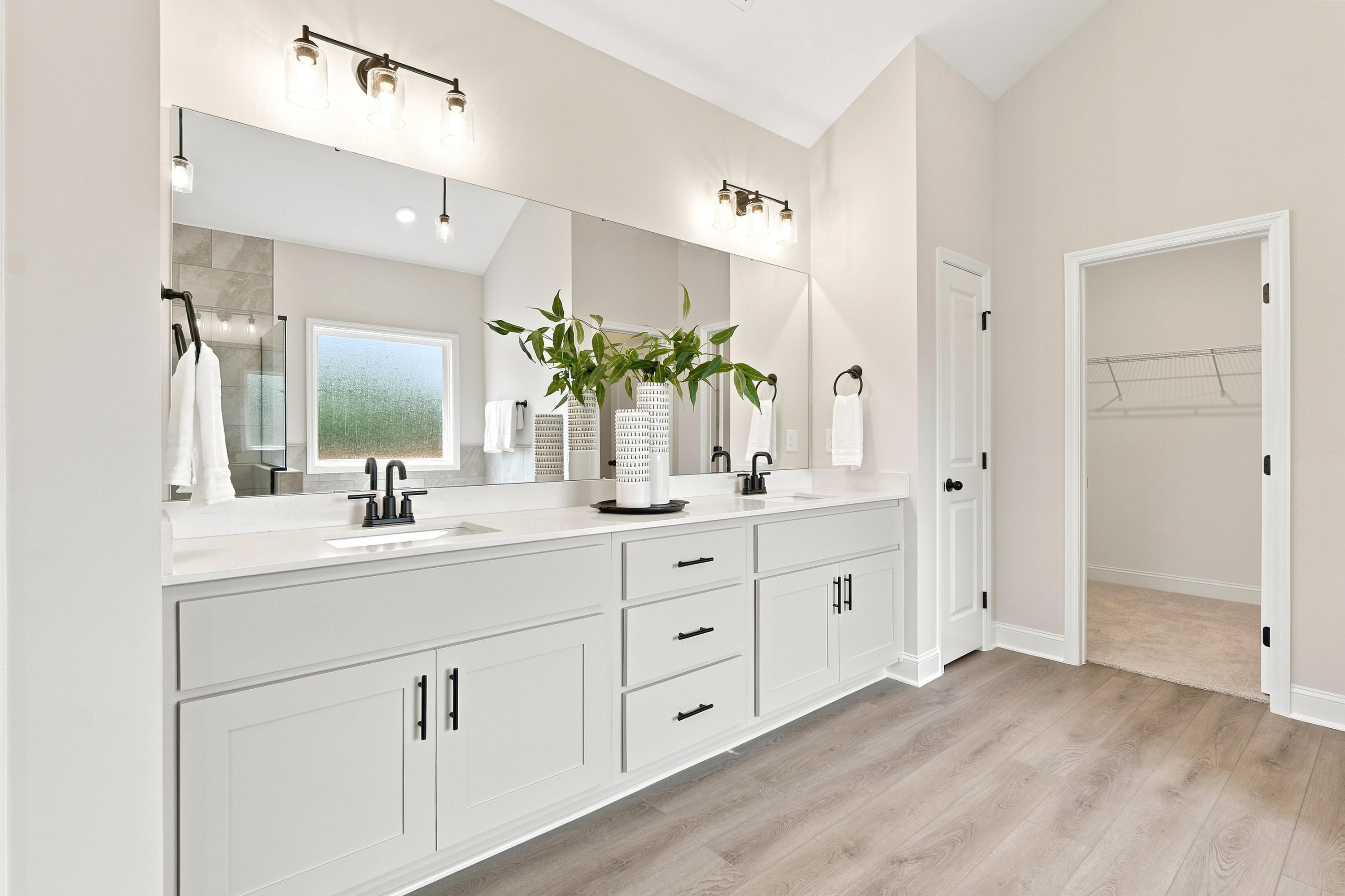 Modern primary bathroom at Riverton Preserve in Huntsville, AL, featuring dual vanities, quartz countertops, and walk-in closet.
