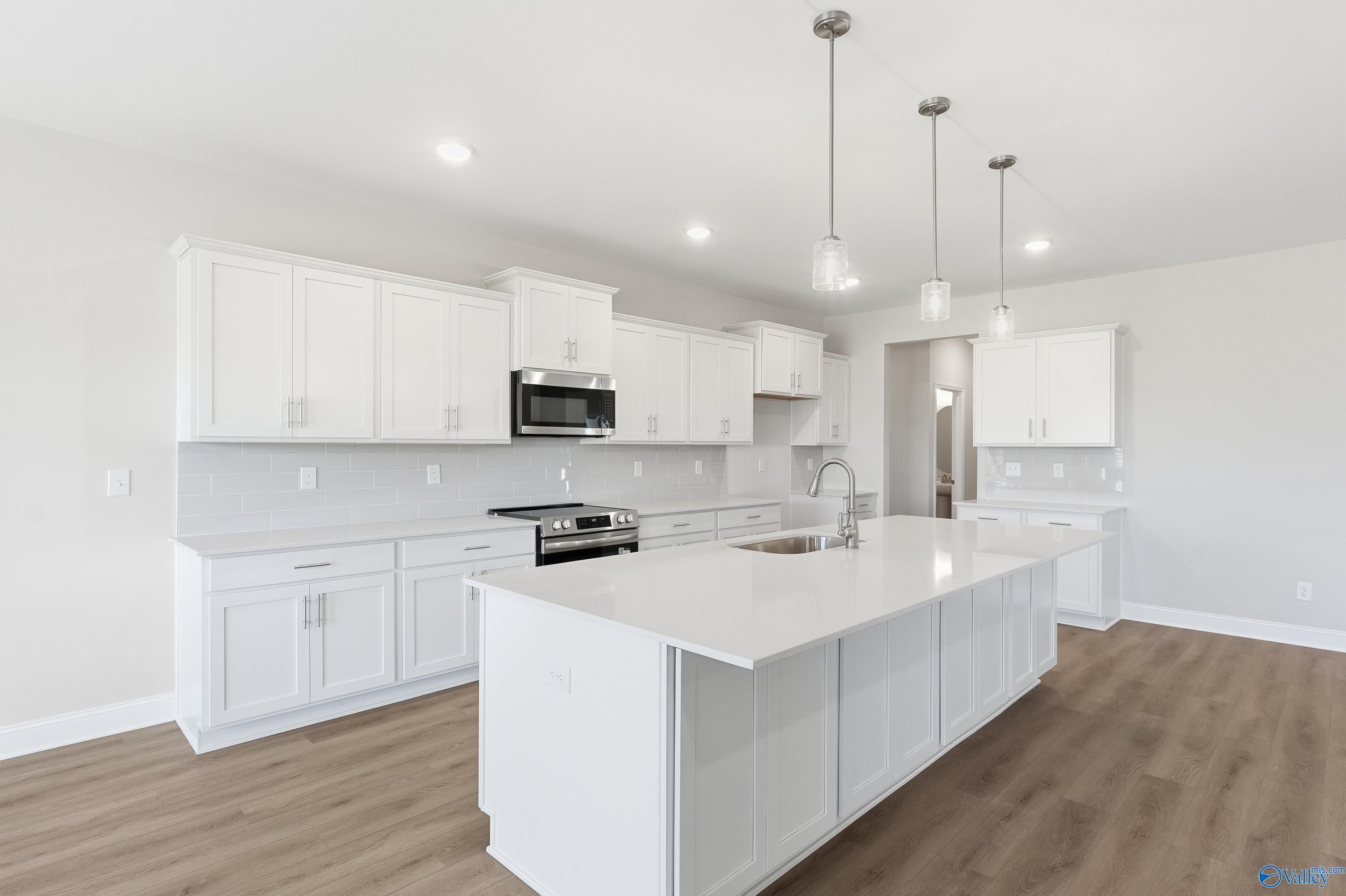 Modern white kitchen with quartz island, stainless steel appliances, and subway tile backsplash in Davidson Homes The Finleigh, Harvest, AL