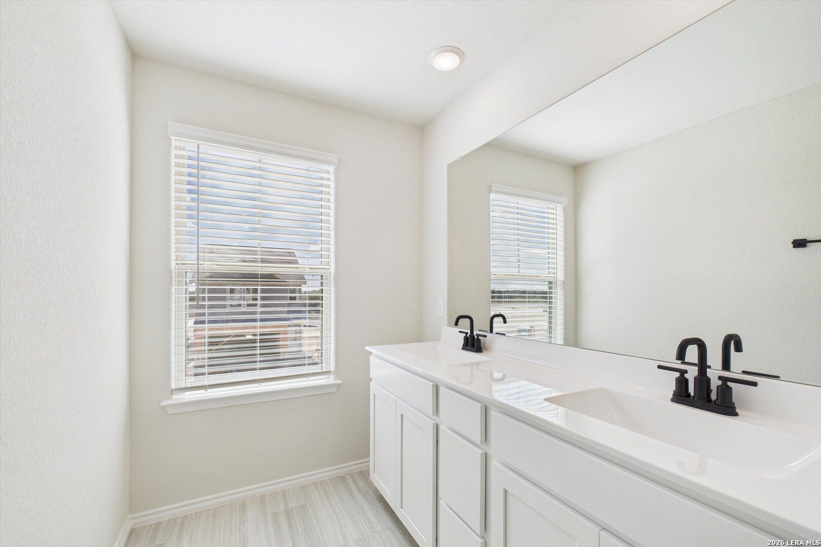 Spacious master bathroom double vanity with white cabinets, black faucets, large mirror, and window in Davidson Homes The Gillian B, San Antonio