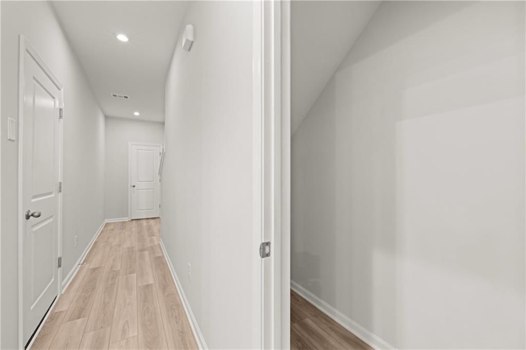 Bright upstairs hallway with light oak floors, white walls, and open door in Davidson Homes The Monroe B, Emerson, Georgia