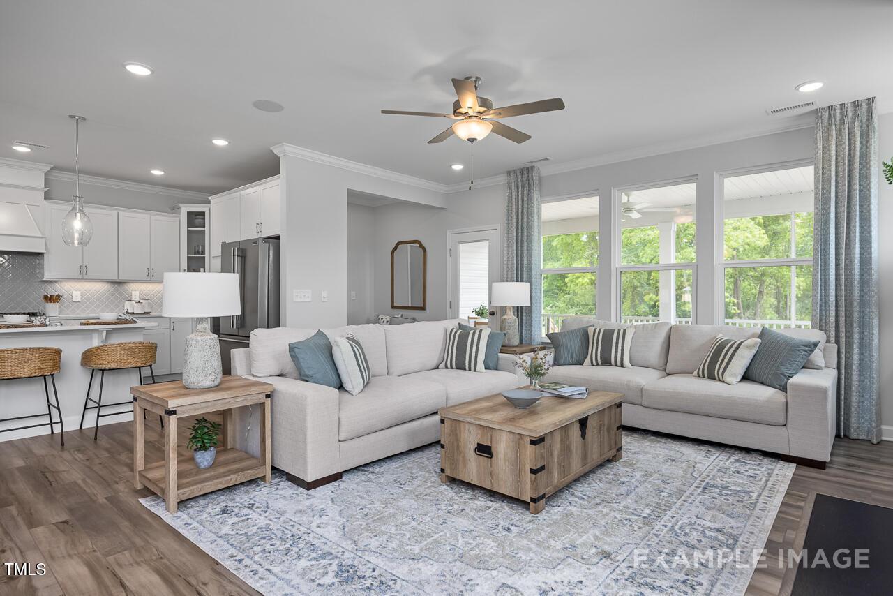 Inviting open living room with L-shaped beige sofa, wooden coffee table, and adjacent white kitchen in Davidson Homes The Magnolia B, Angier, NC