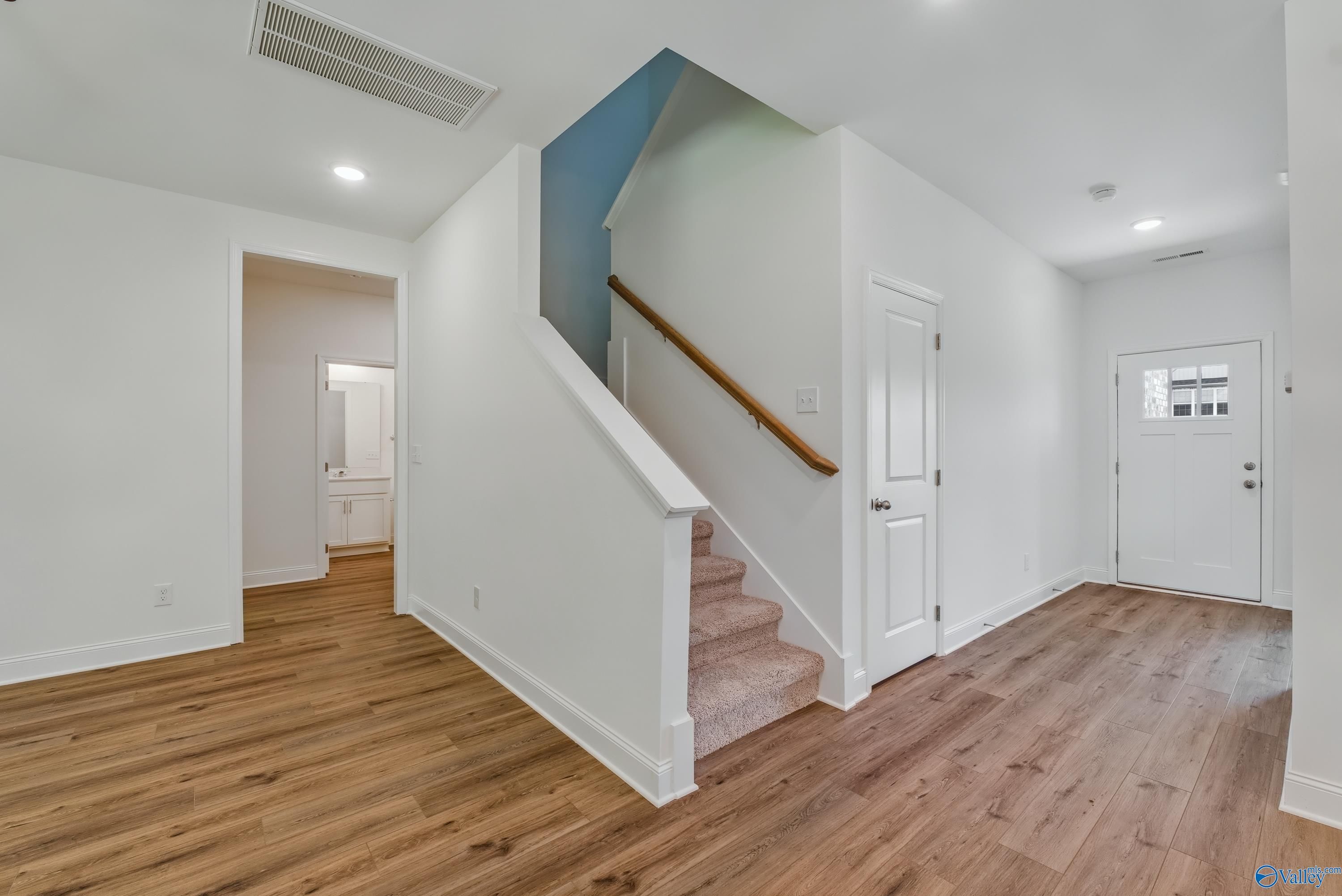 Welcoming foyer with wooden floors, open powder room, grand staircase, and front door in Davidson Homes The Shelby A, Arab, Alabama