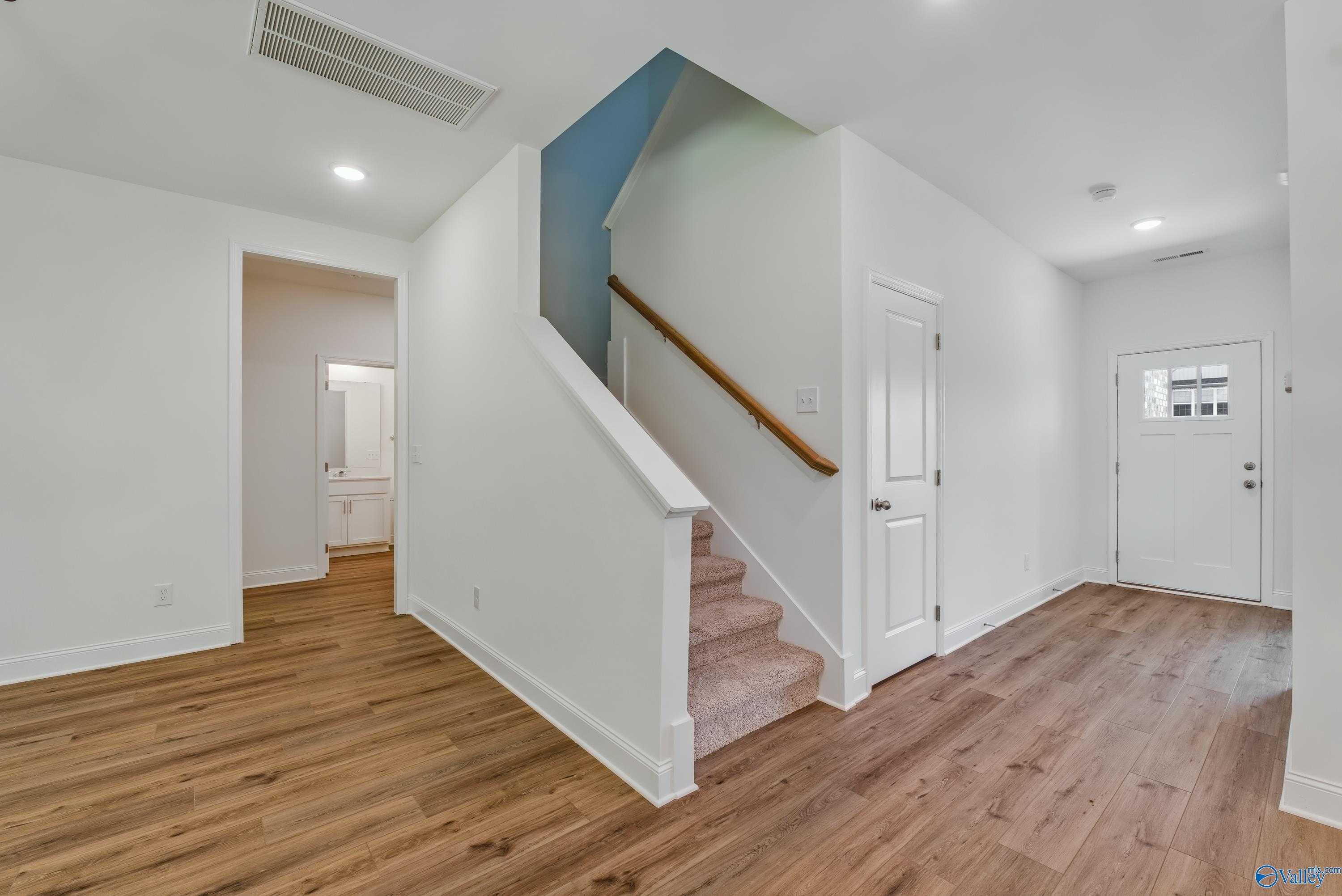 Welcoming foyer with wooden floors, open powder room, grand staircase, and front door in Davidson Homes The Shelby A, Arab, Alabama