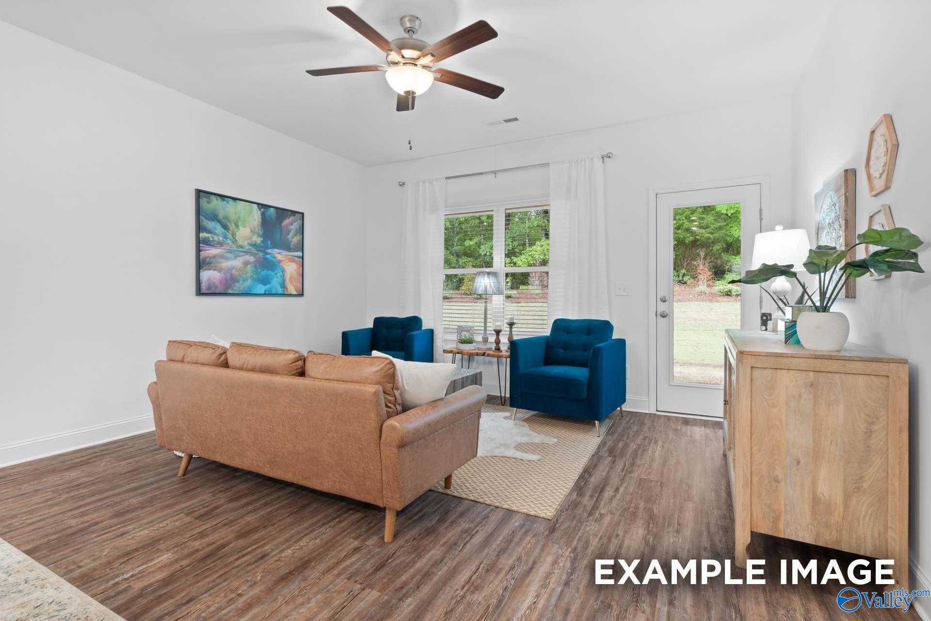 Cozy living room featuring tan leather sofa, blue velvet chairs, ceiling fan, large windows and sliding door to backyard in Davidson Homes The Cumberland, Decatur, Alabama