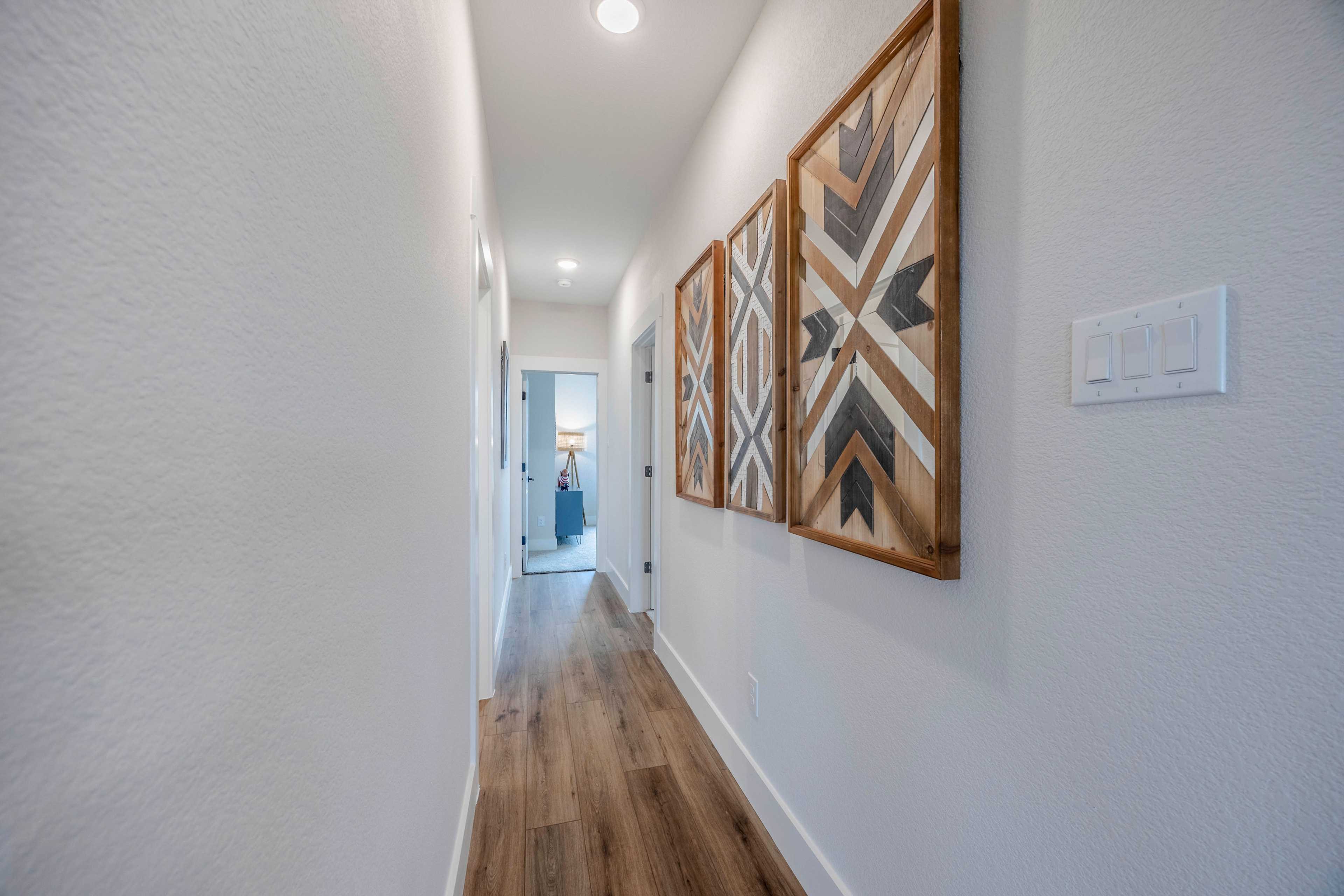 Spacious hallway in The Rockford home design with hardwood floors, white walls, recessed lights, and geometric wooden wall art