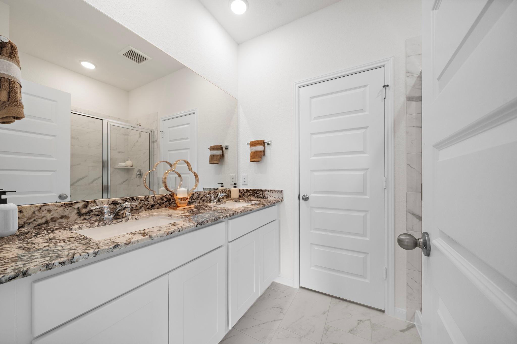 Spacious primary bathroom at The Villages at WestPointe in Dayton Texas with double vanity granite counters and frameless glass shower