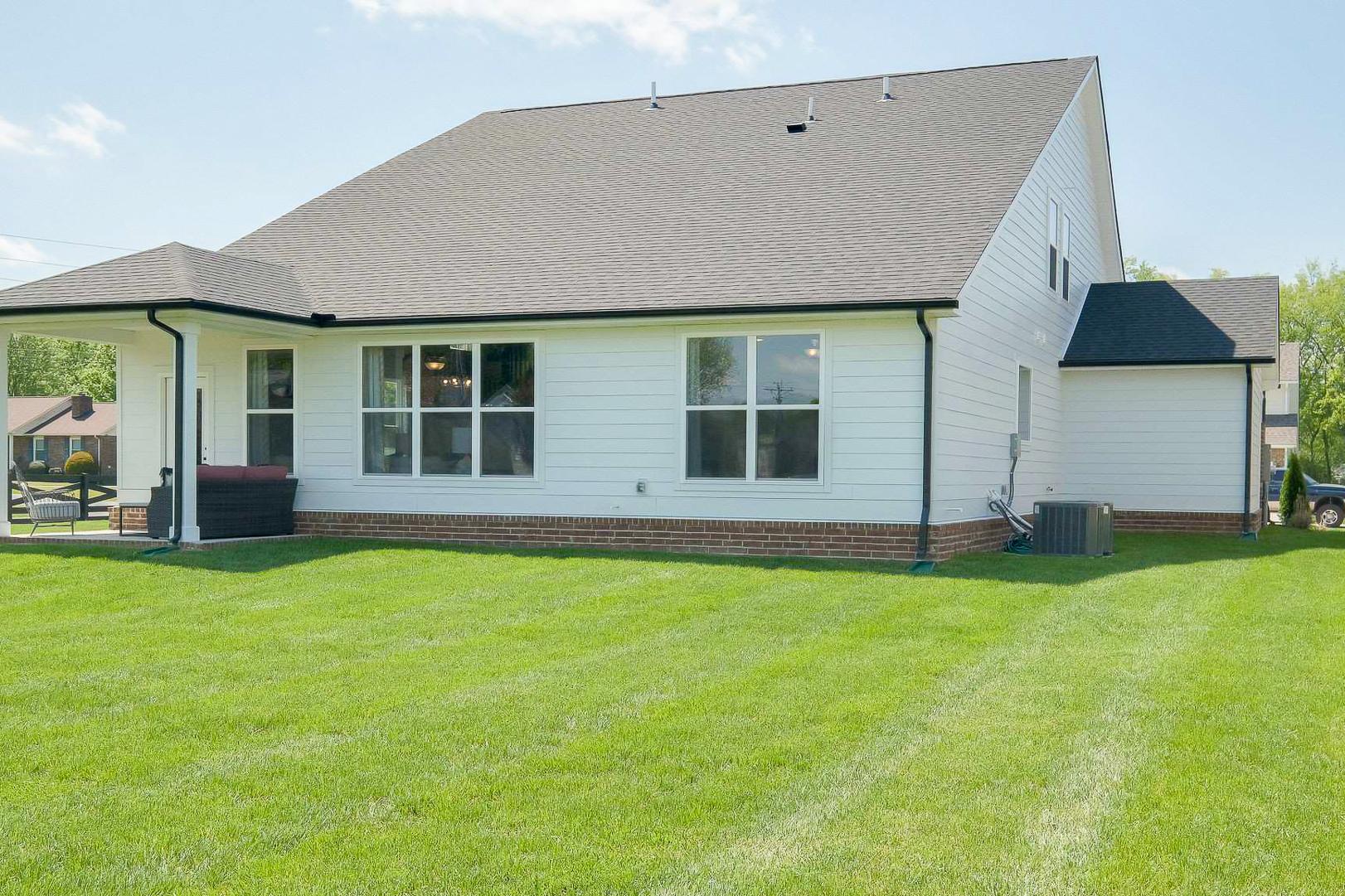 Modern single-story home backyard with covered patio, hot tub, large windows, and lush lawn at The Meadows in Smyrna, Tennessee by Davidson Homes