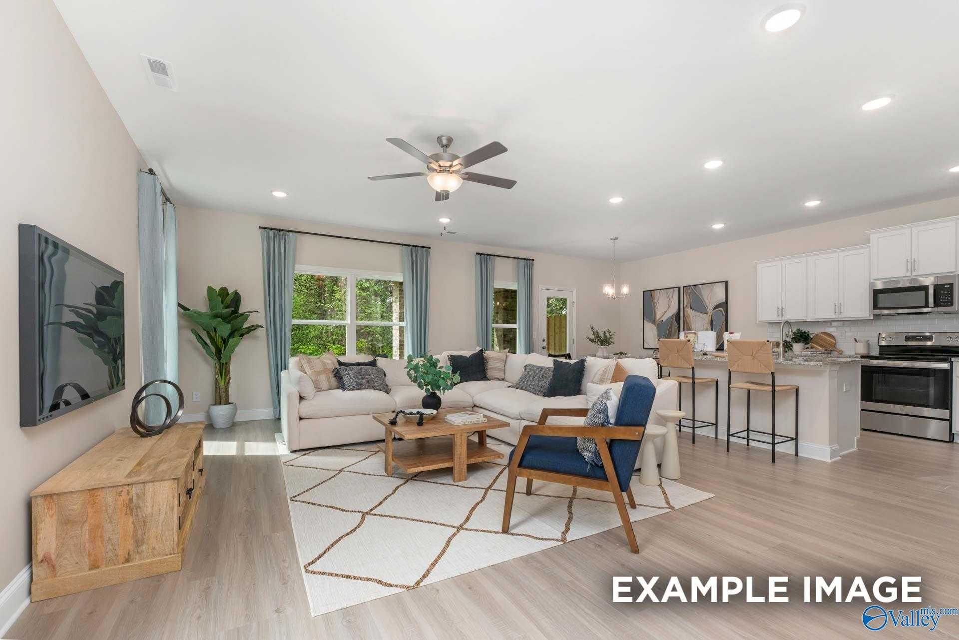 Open-concept living room with plush beige sofa, TV, plants, and ceiling fan flowing into white kitchen in Davidson Homes The Camden B, Huntsville, AL
