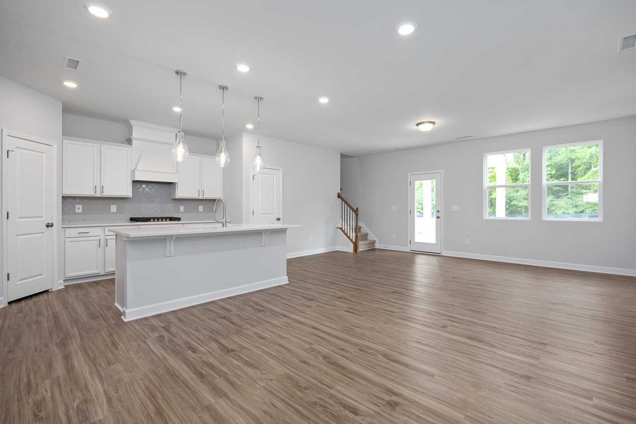 Open-concept kitchen and living area in The Durham D home with white cabinets, large island, hardwood floors, and staircase