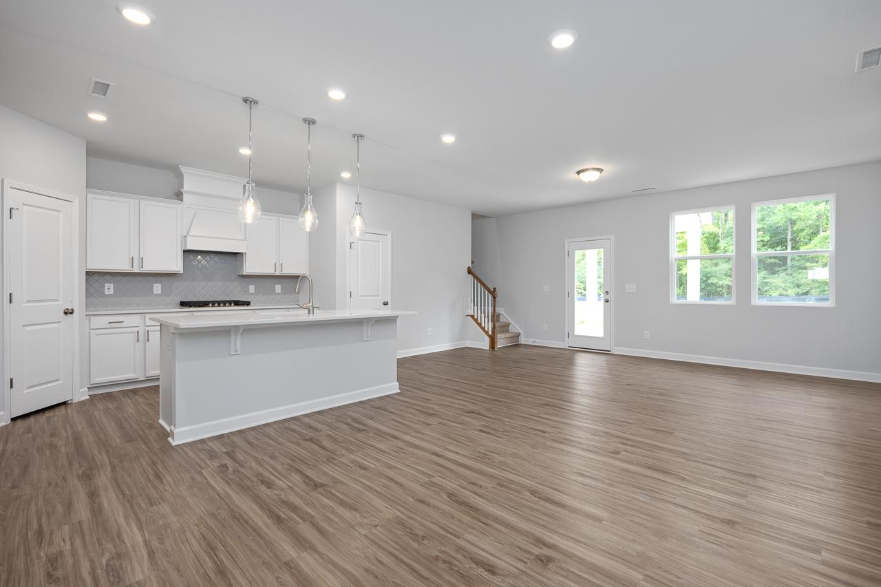 Open-concept kitchen and living area in The Durham C home with white cabinets, quartz island, pendant lights, hardwood floors, and staircase