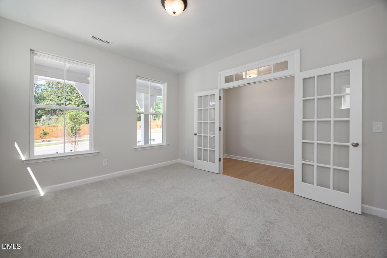 Bright home office with French doors and carpeted flooring in The Ashport L floor plan at Sage on North Main, Wake Forest.