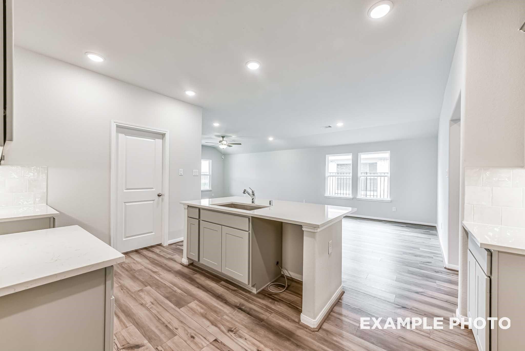 Open-concept kitchen with center island and wood-plank flooring in The Laguna C by Davidson Homes, Sunterra, Katy, Texas.