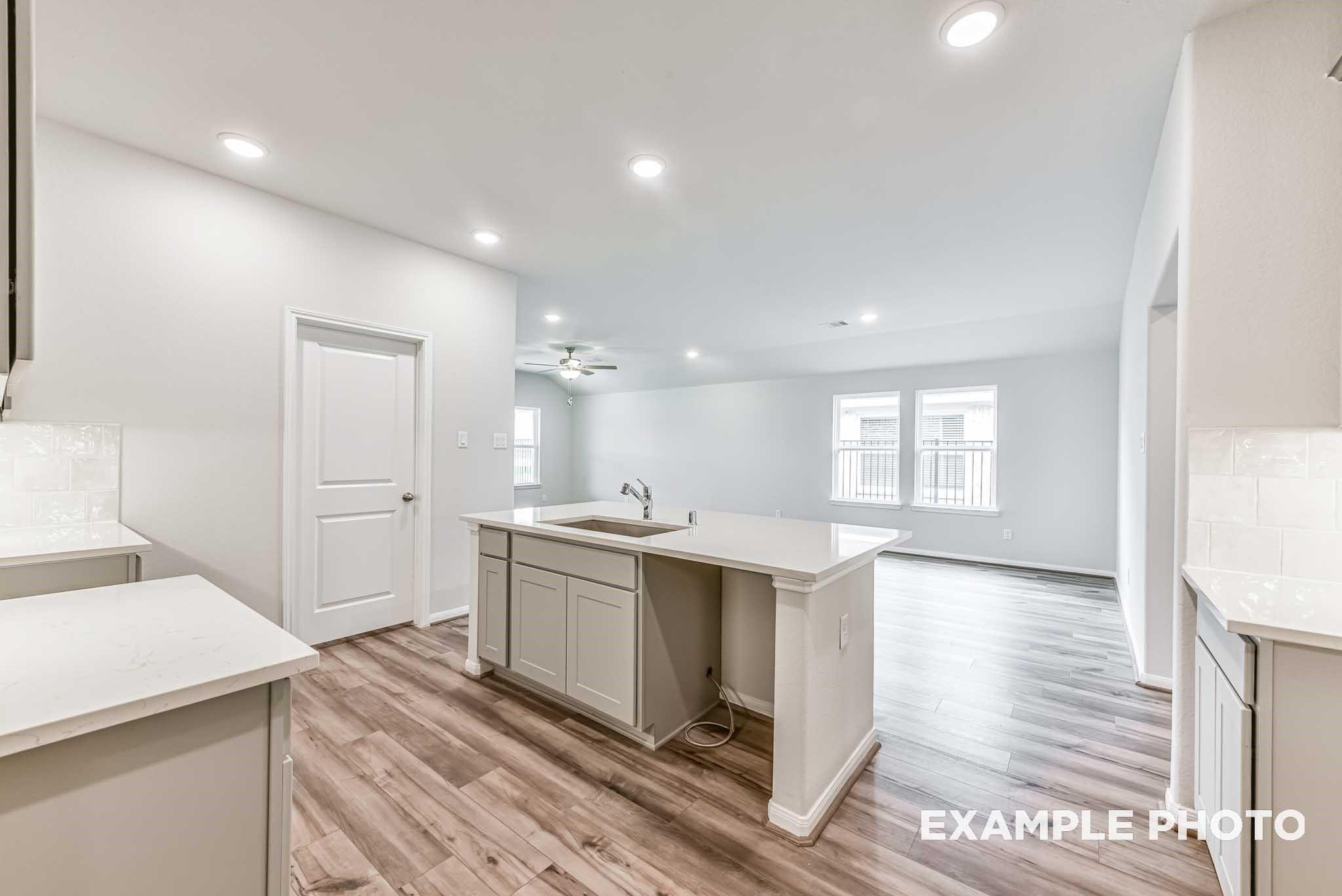 Open-concept kitchen with center island and wood-plank flooring in The Laguna C by Davidson Homes, Sunterra, Katy, Texas.