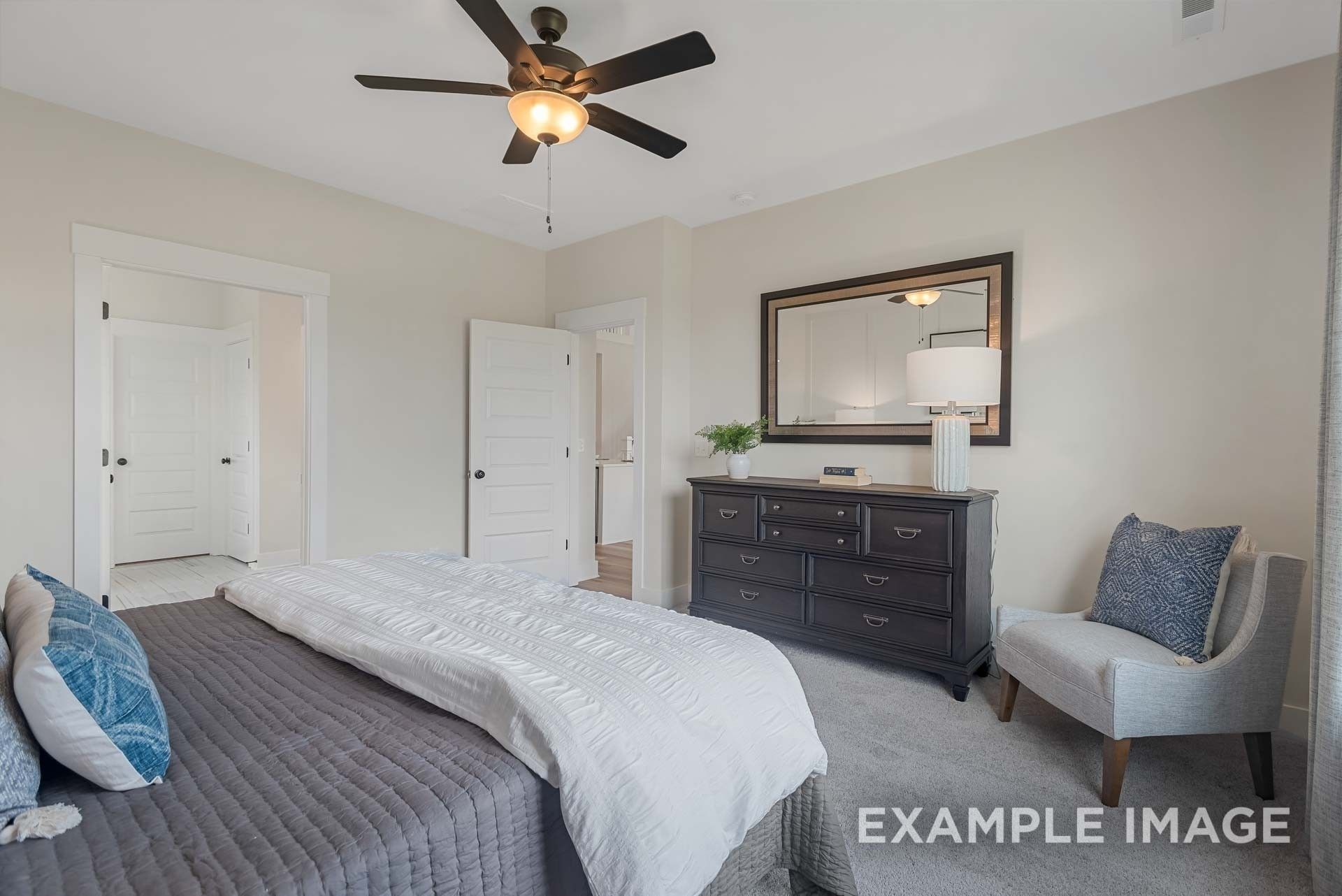 Elegant master bedroom with king bed, dark dresser, large mirror, accent chair, and en-suite door in Davidson Homes Ridgeport C, Gallatin, TN