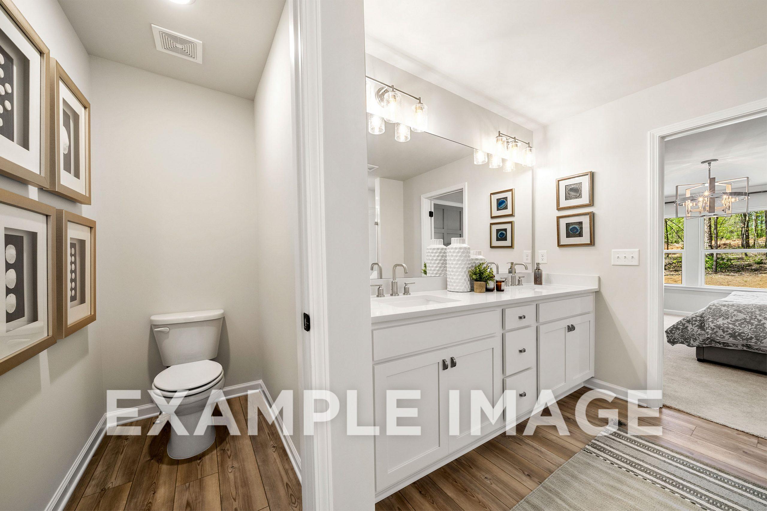 Spacious master bathroom in The Hickory B with double vanity, frameless mirror, toilet, and adjacent bedroom view