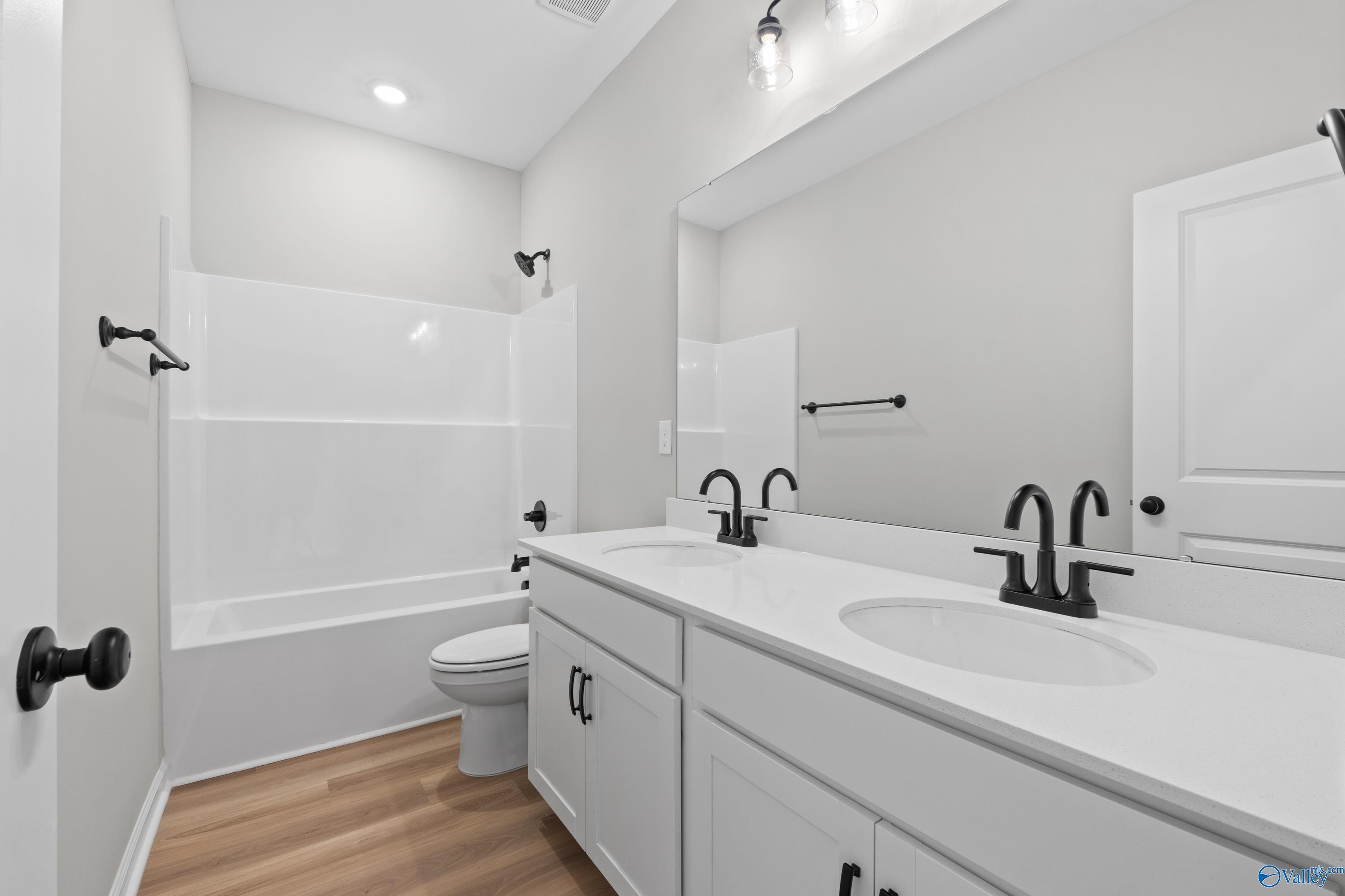 Modern guest bathroom with double white vanity, tub-shower combo, toilet, and hardwood floors in Davidson Homes The Phoenix, Hazel Green, AL